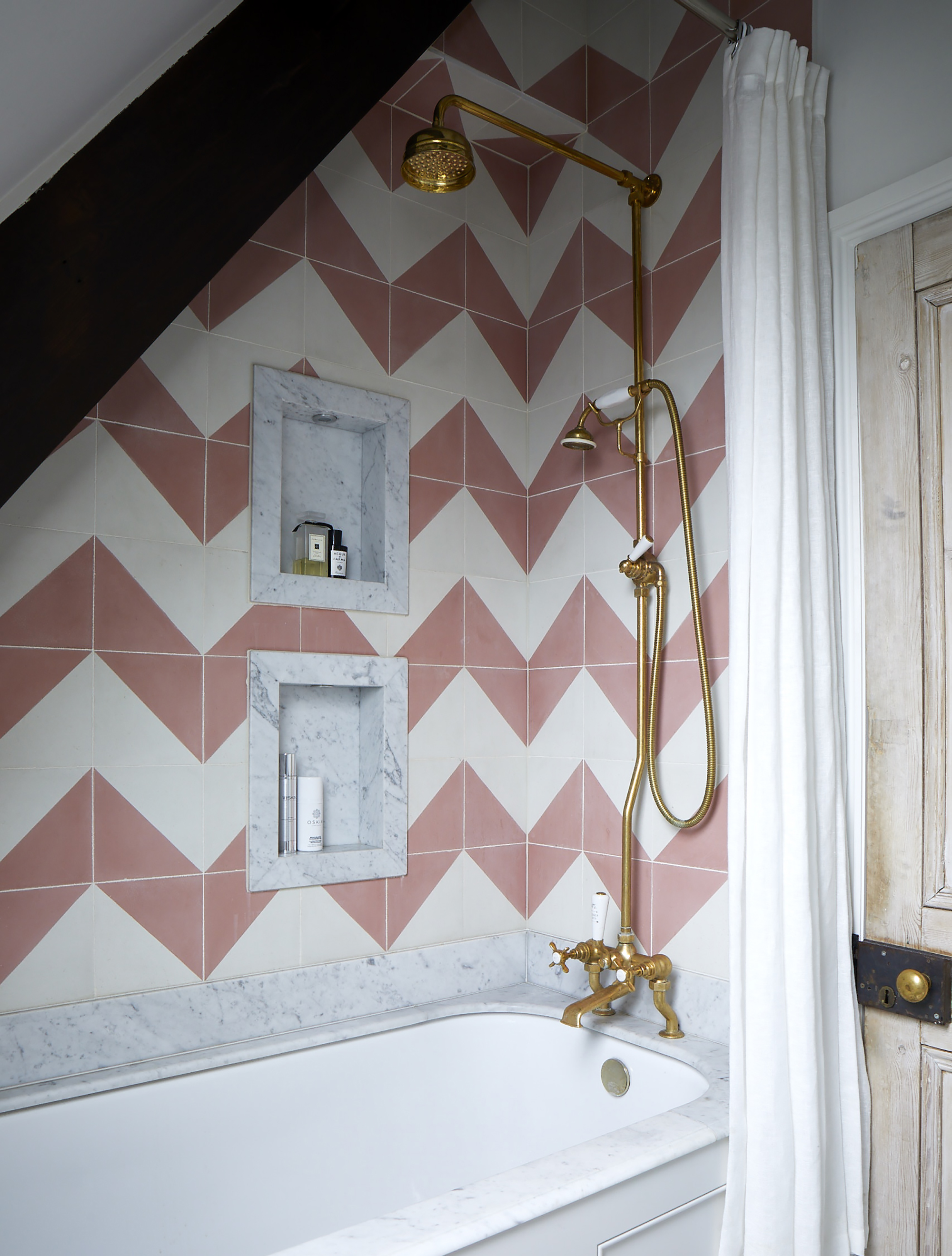 lite bad med innebygd badekar med gull messing og rosa og hvite chevron fliser på veggen