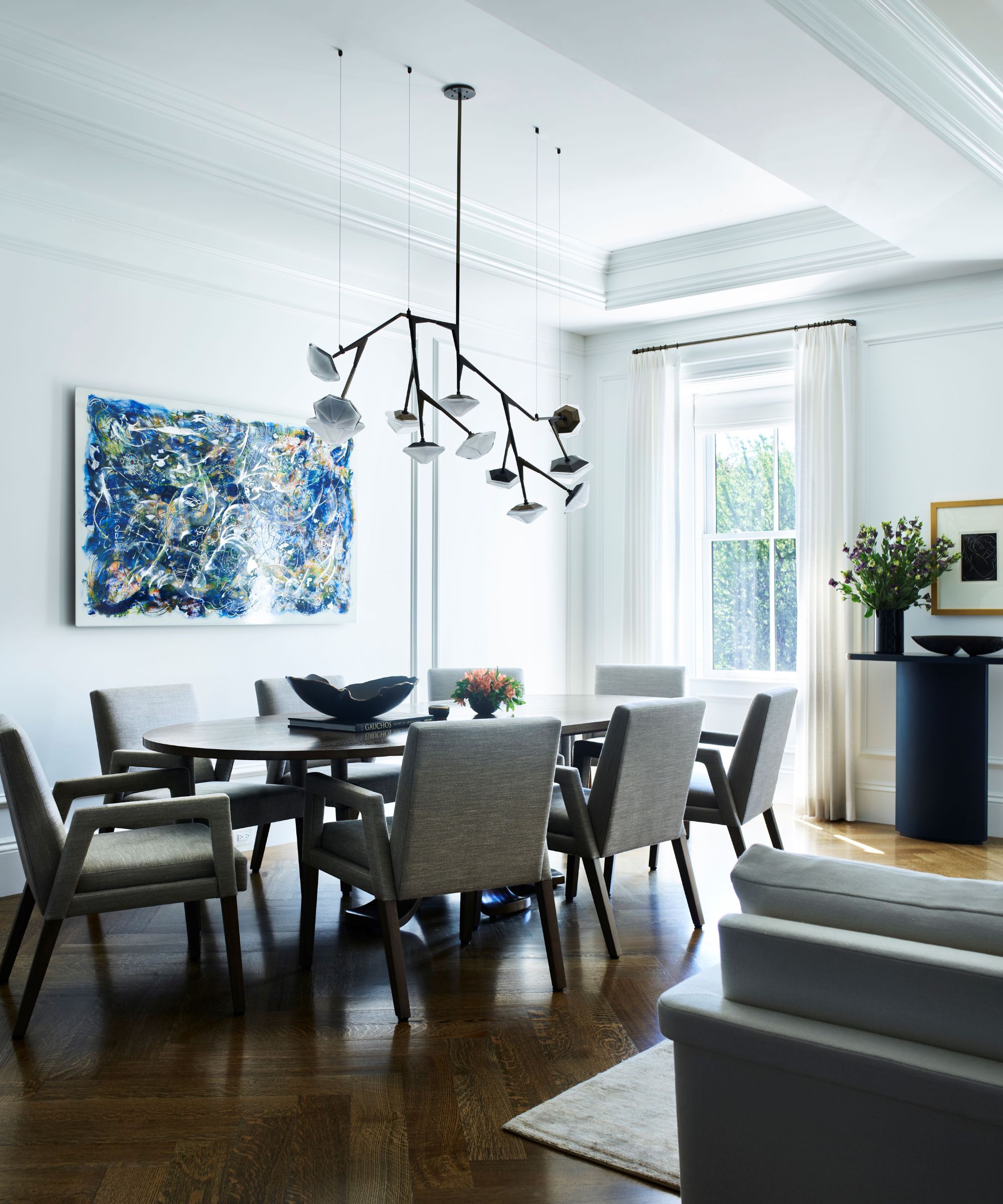 spisestue med ovalt bord og polstrede stoler og blå kunst og moderne lysekrone i glass