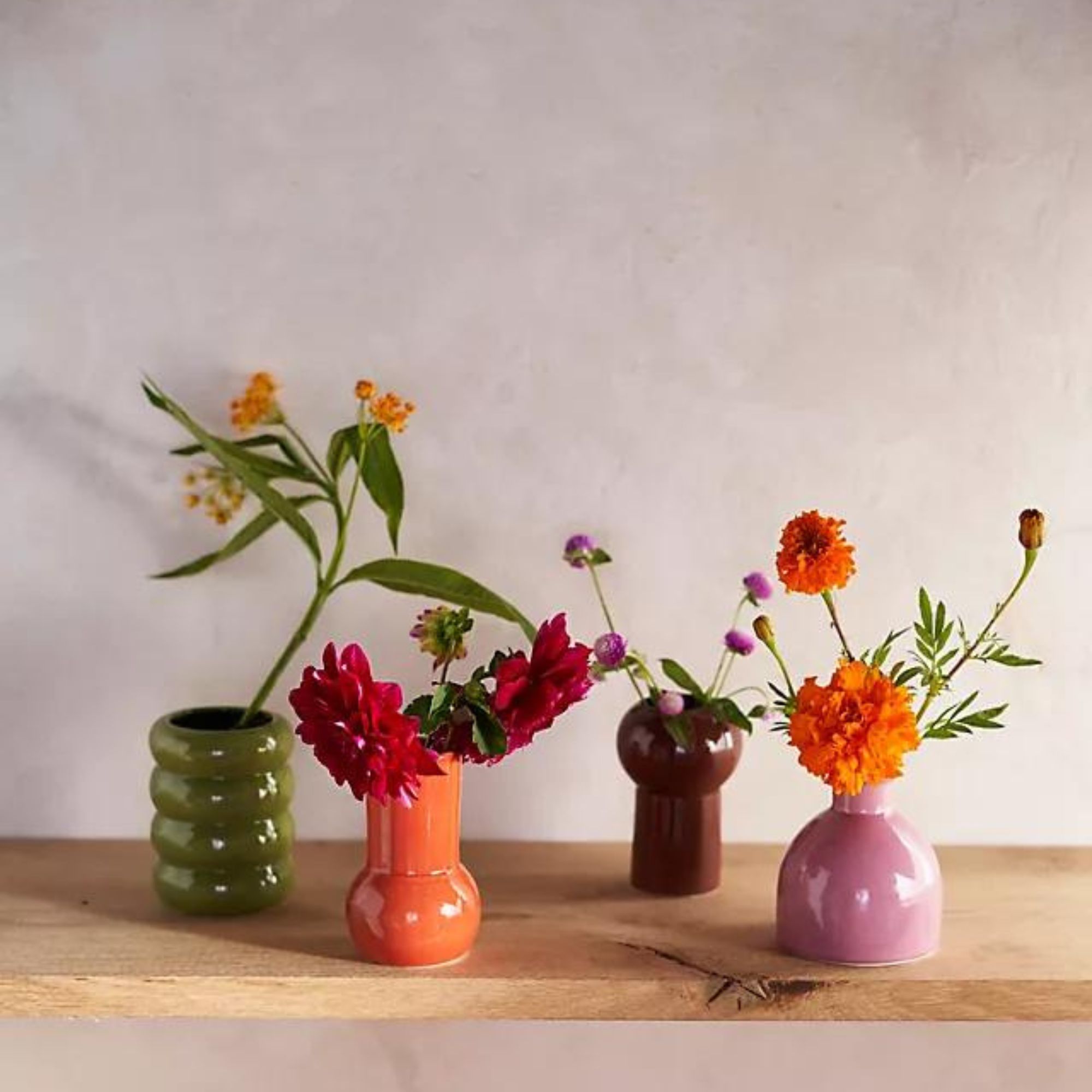 Fire fargerike vaser med blomster på en trehylle