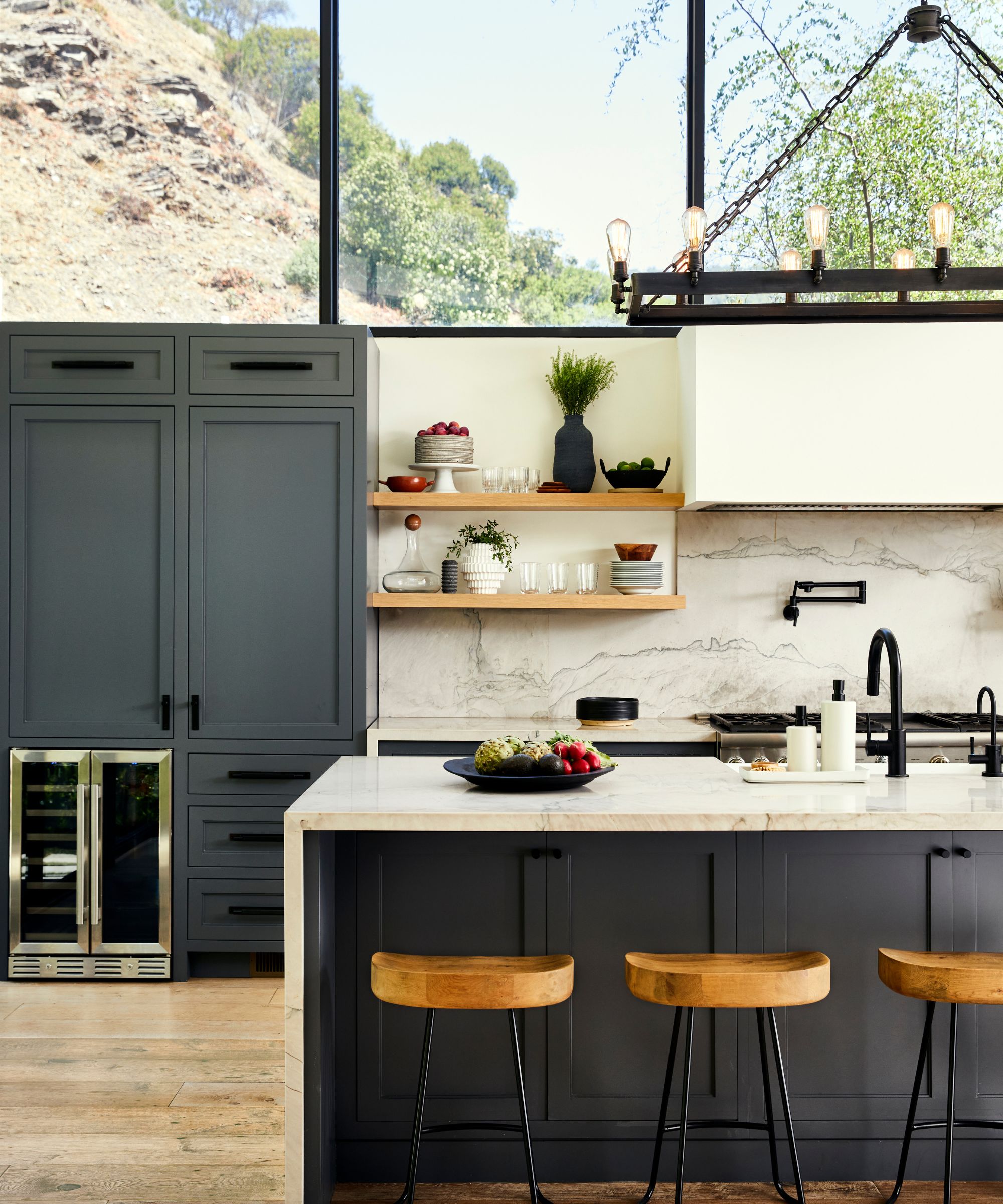 kjøkken med blå enheter og marmor toppet øy og backsplash og høye vinduer