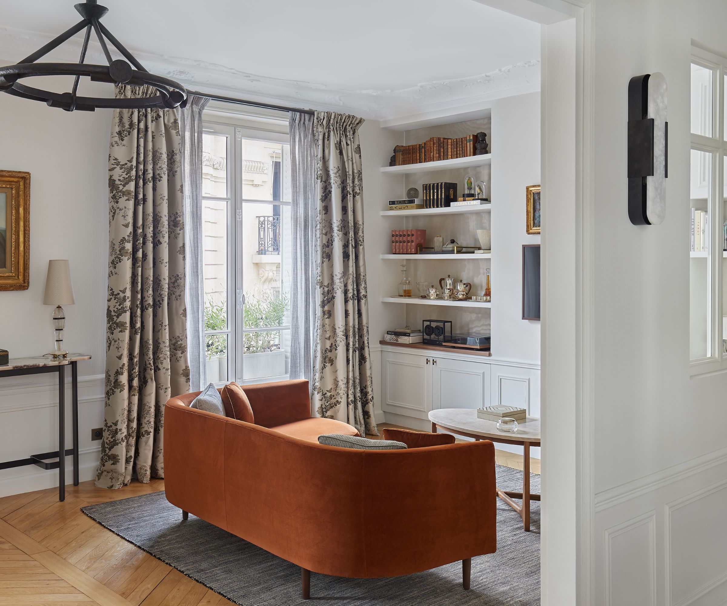 stue med skillevegg og russet sofa og tidstypiske vinduer med mønstrede gardiner og hvite vegger