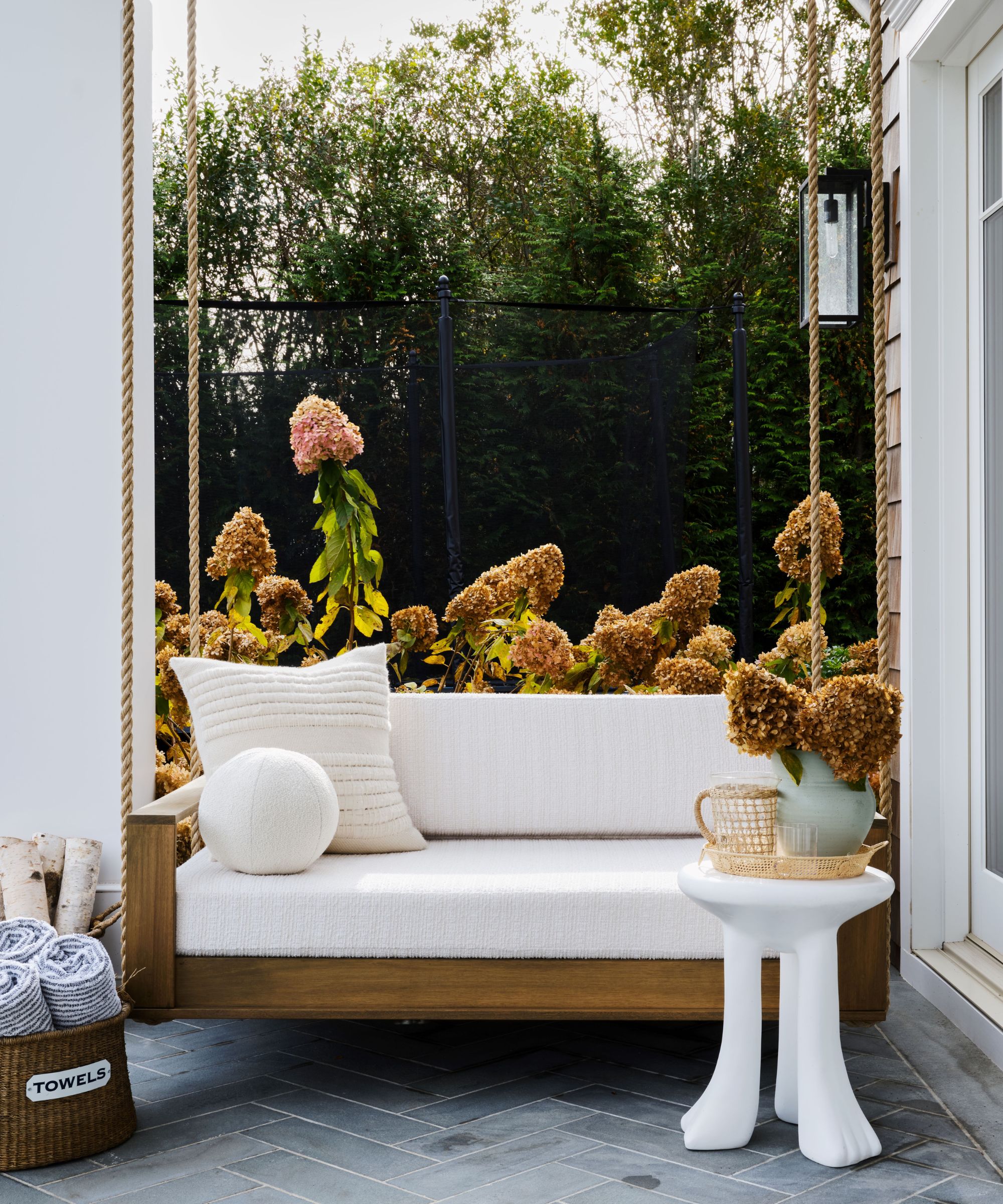 veranda med hvit sofa, hvite puter og hvitt sidebord med hageblomster i bakgrunnen