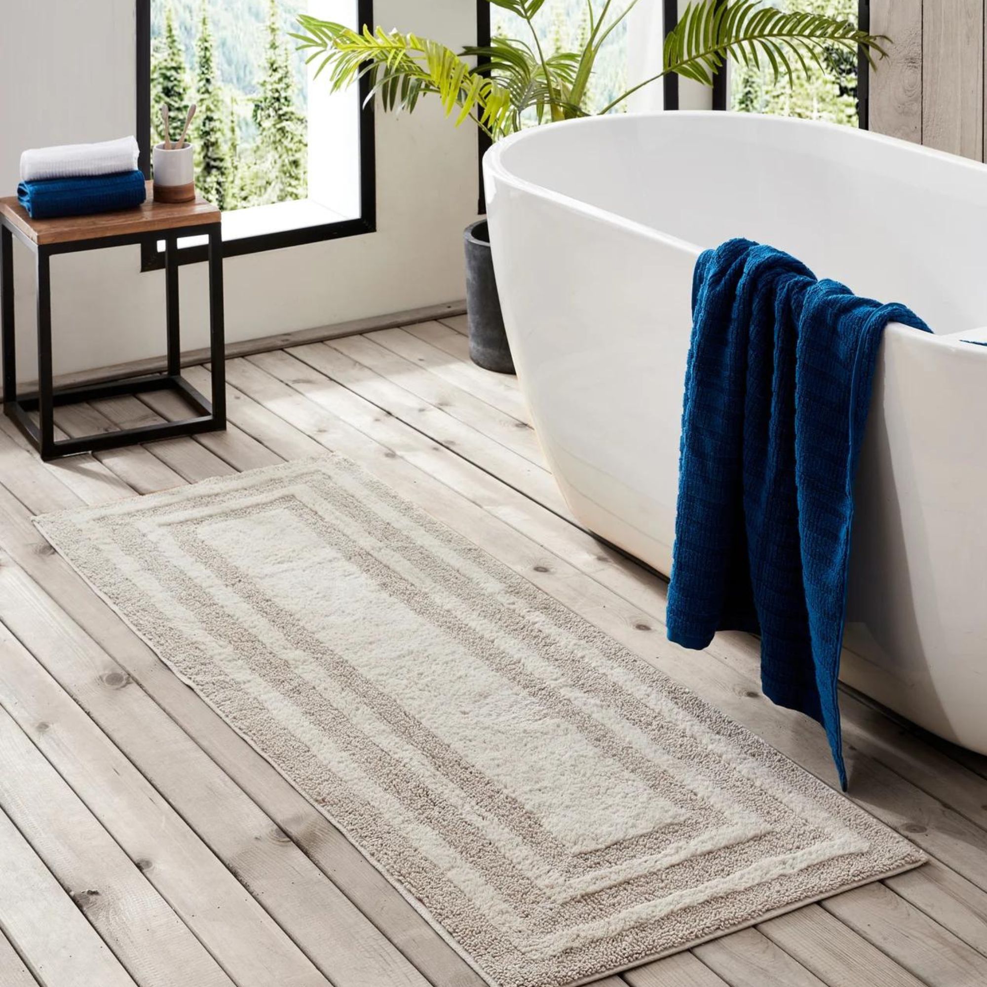 Eddie Bauer Logan Bath Rug Runner i bomull ved siden av et hvitt buet frittstående badekar. Et mørkeblått håndkle drapert over siden.