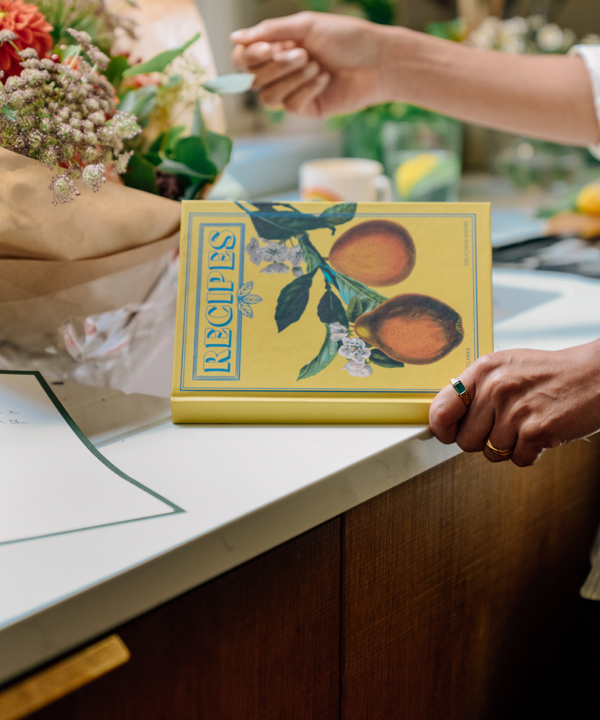 bilde av oppskriftsbok på hvit benkeplate som holdes, innpakket blomster ved vasken