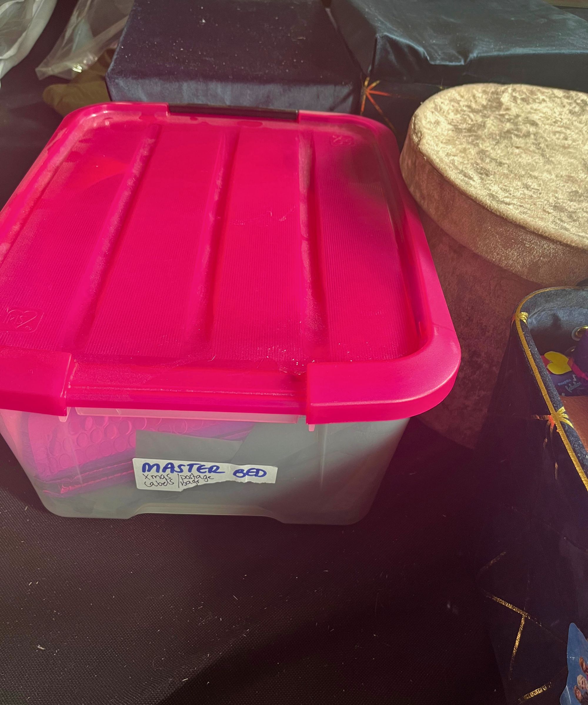 Oppbevaringsboks i gjennomsiktig plast med rosa lokk og en etikett som viser master bed Xmas innpakning og konvolutter