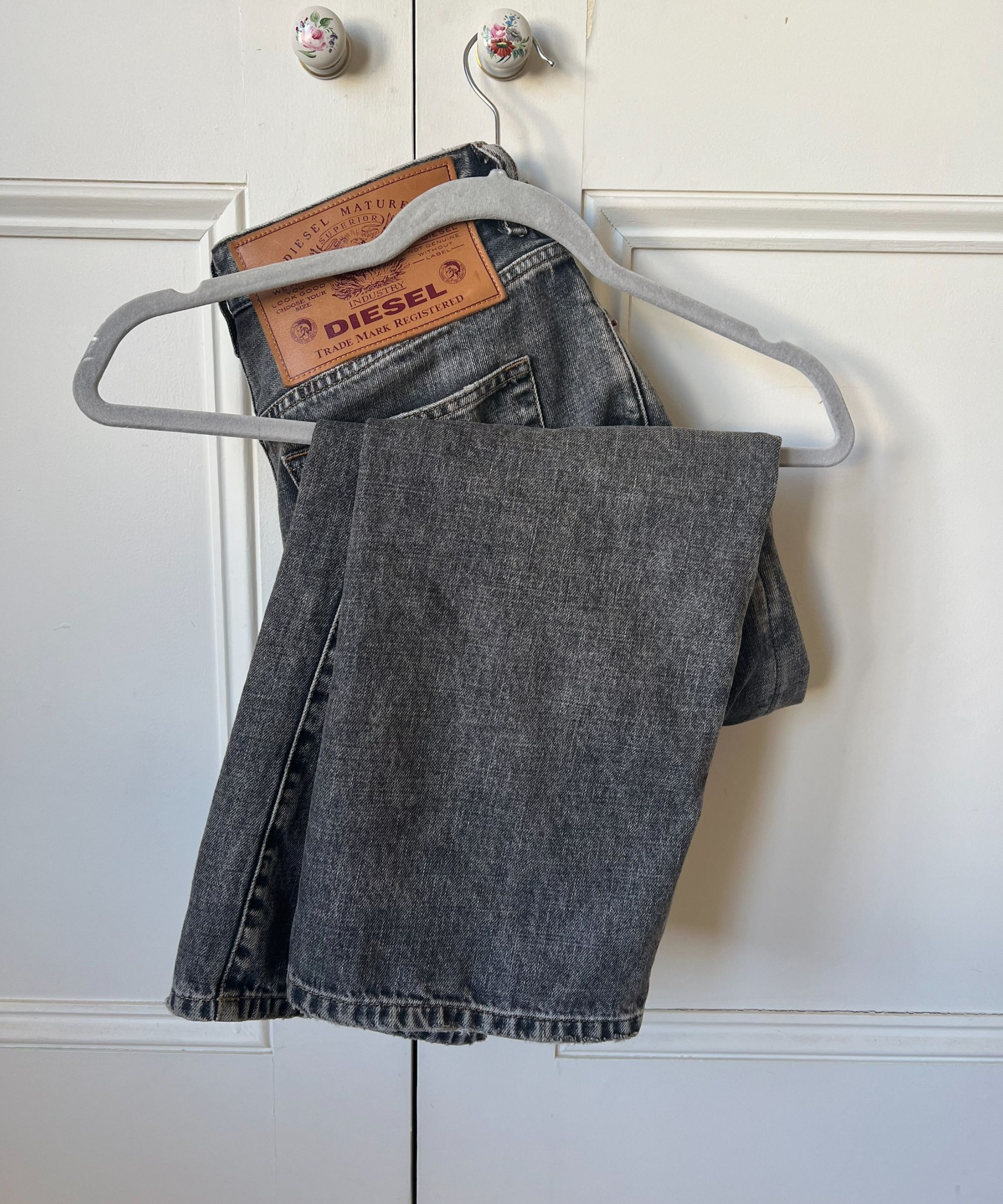 Et par grå Diesel-jeans på en grå fløyelshenger som henger på en dørhåndtak i et blomsterskap