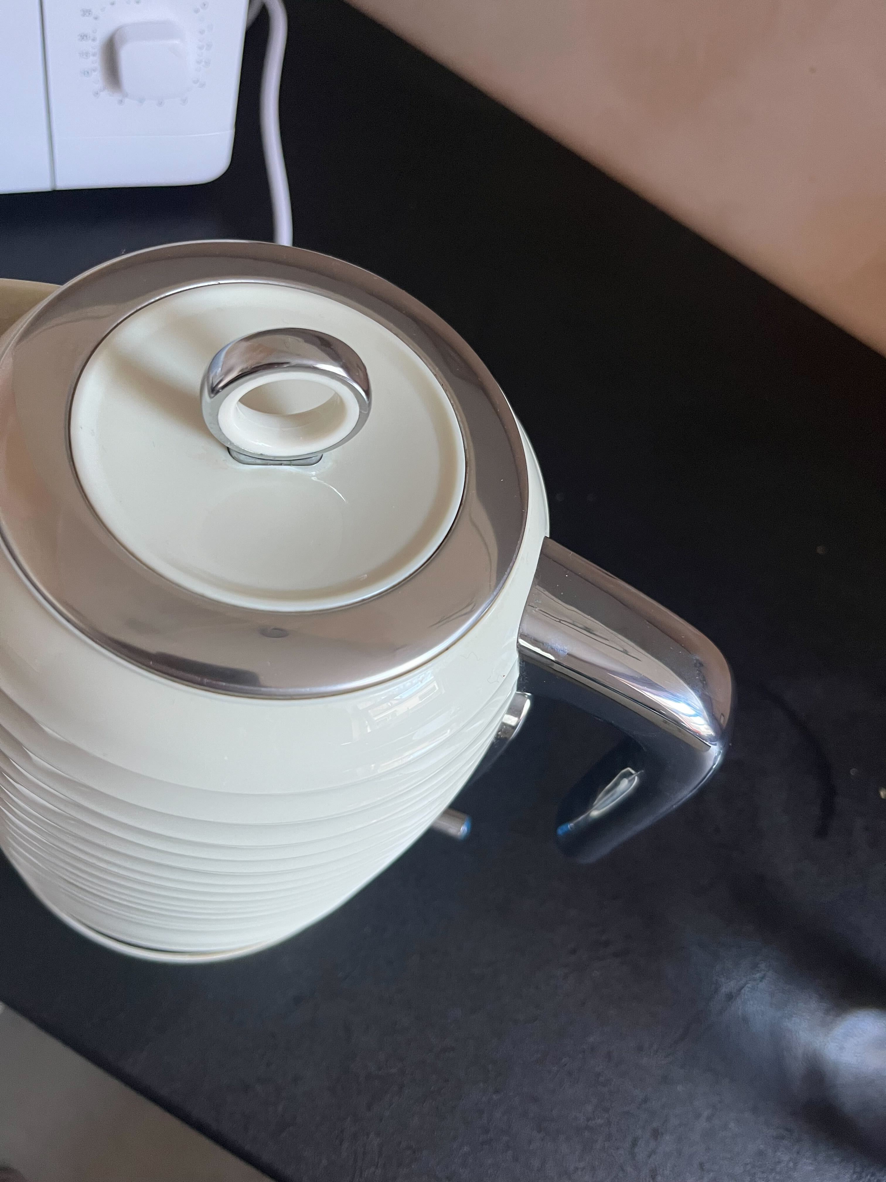 En kremkjele med kant i rustfritt stål foran en hvit mikrobølgeovn på en svart benke