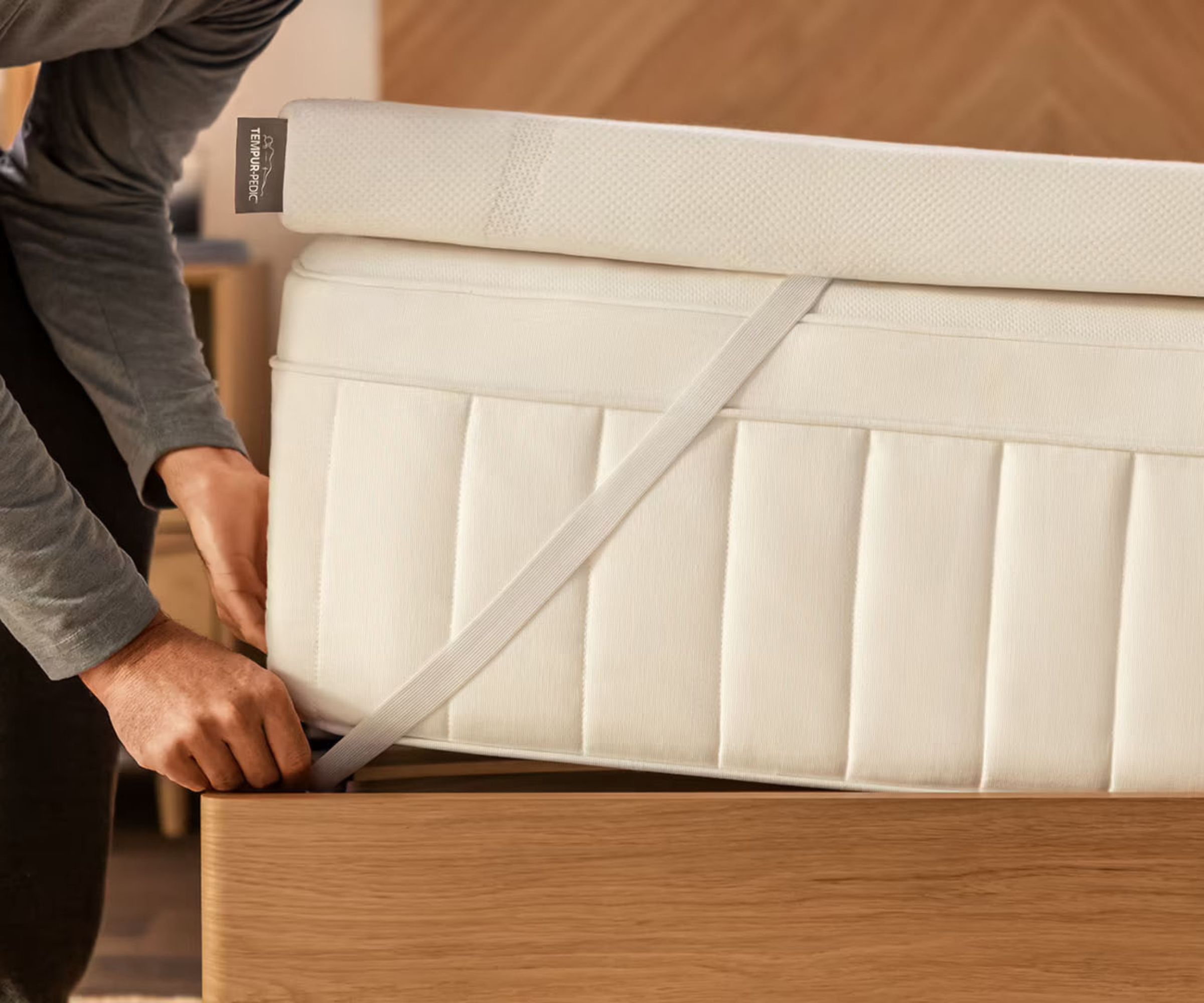 En mann som trekker hjørnestroppen til en Tempur-Pedic Tempur-Adapt over en Tempur-Pedic-madrass