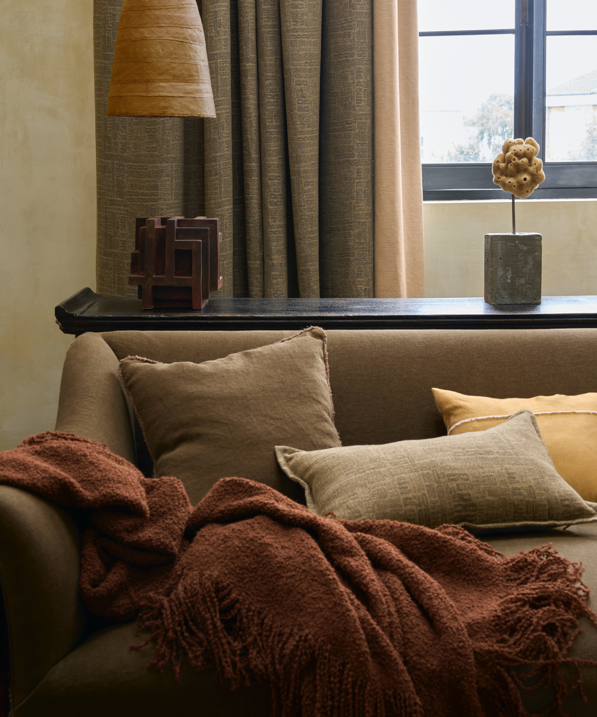 nøytral stue med mokka sofa med rustkast, sengeputer, mahogni konsoll bak, taupe/grå gardiner, lamper, gjenstander