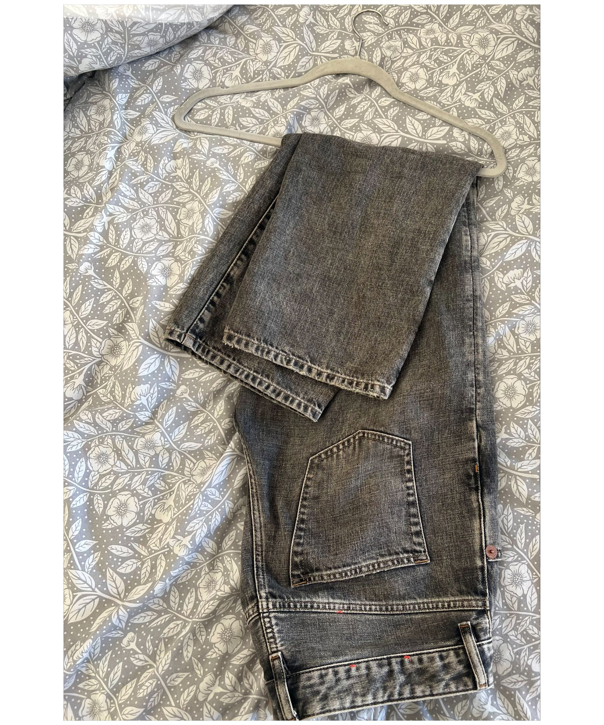 Et par mørkegrå jeans brettet på en grå fløyelshenger på en grå blomsterdyne