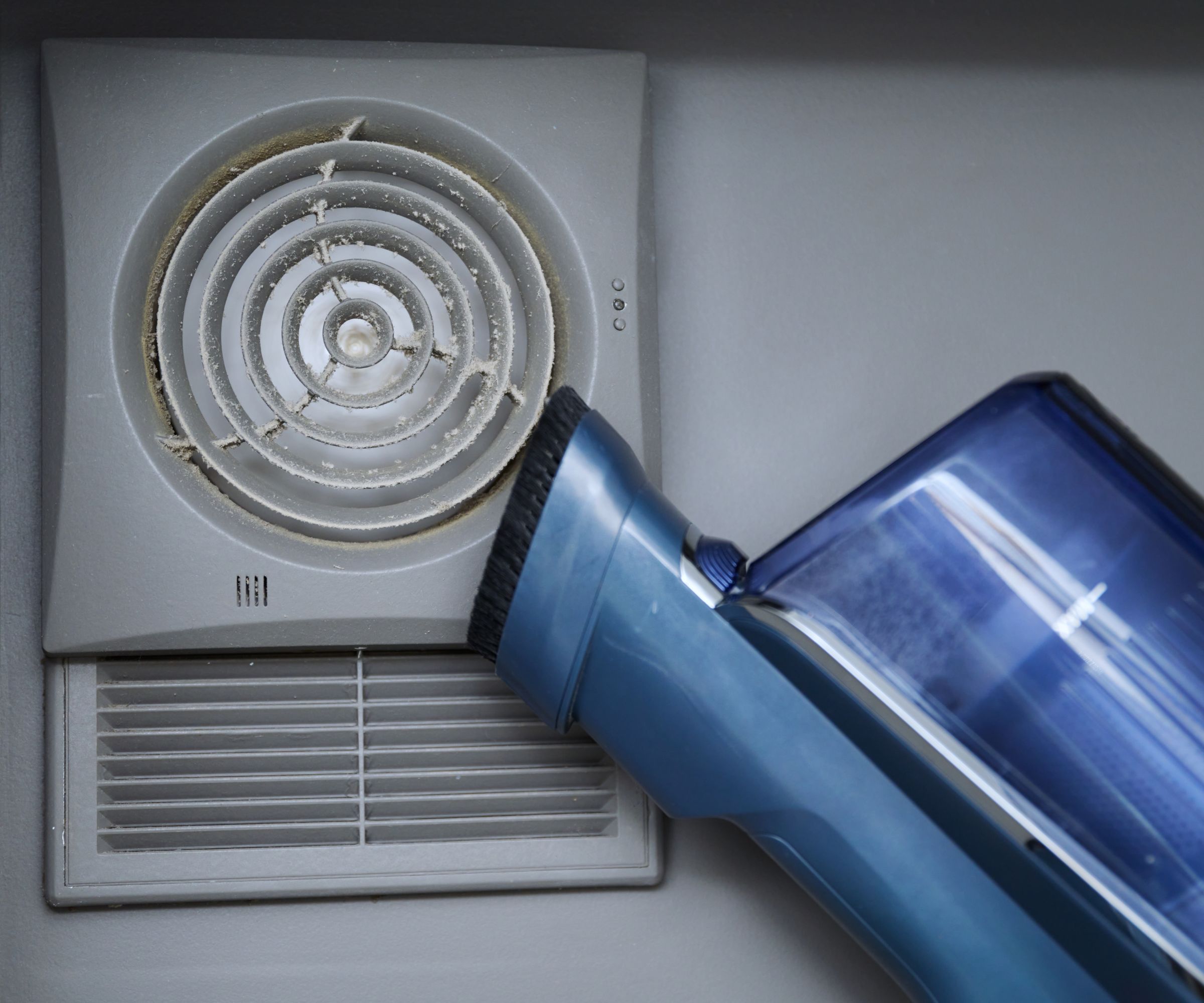 Rengjøring veggmontert støvete hette ventilasjonsgrill på bad med støvsuger.