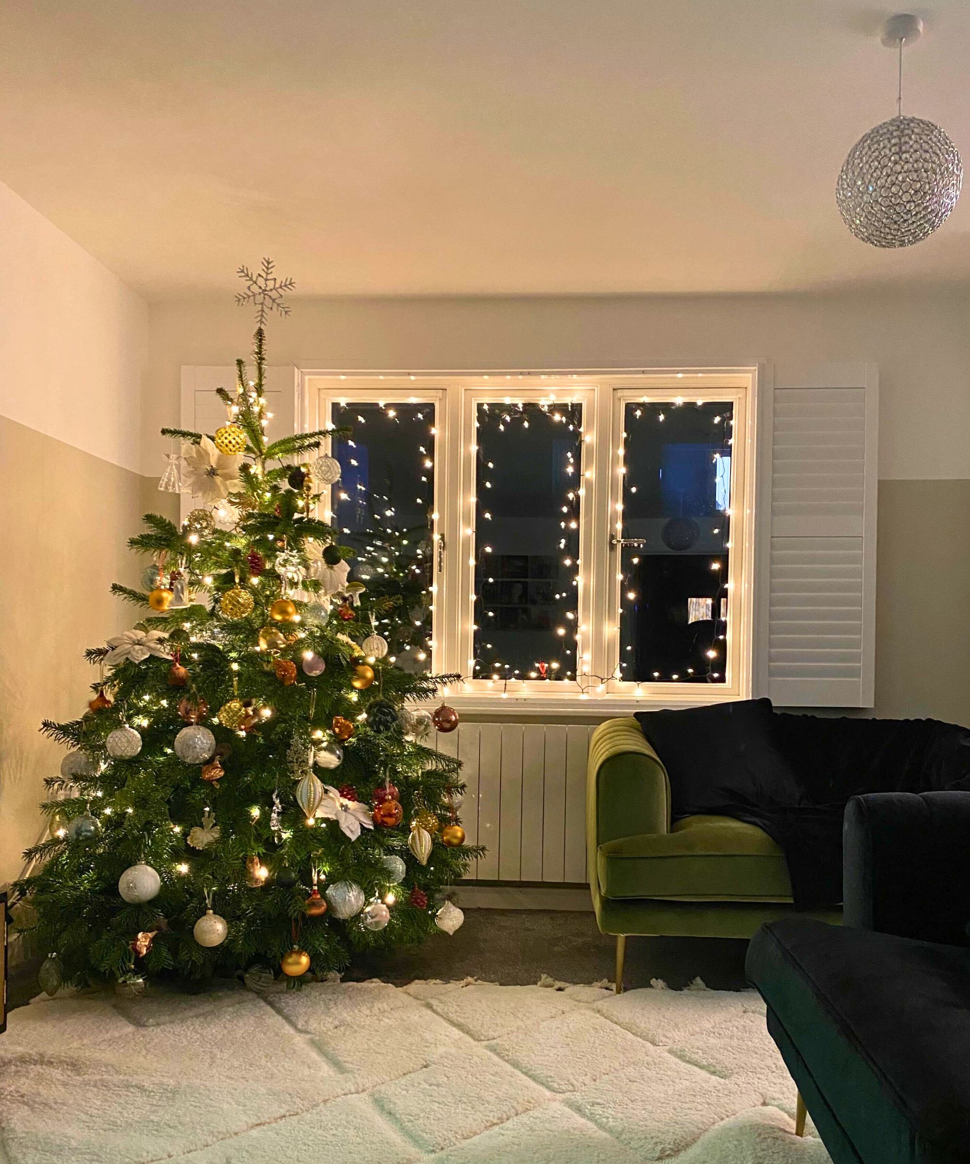 En stue med kremteppe svarte og grønne fløyelssofaer og et stort naturlig juletre med lys og høstkuler