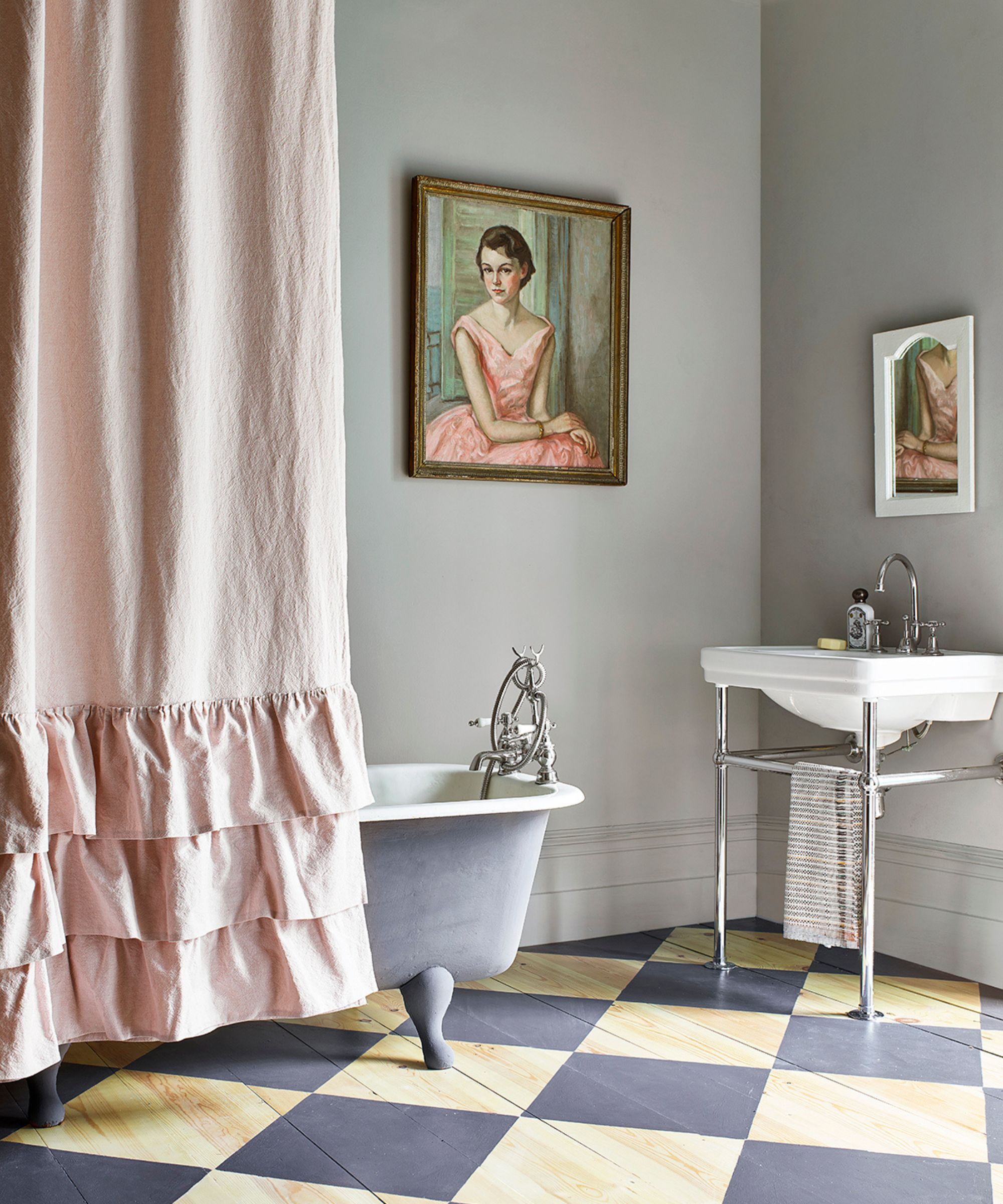 bad med grå vegg, rutete gulv, opprullbar badekar med rosa rynket dusjforheng og kunstverk på vegger