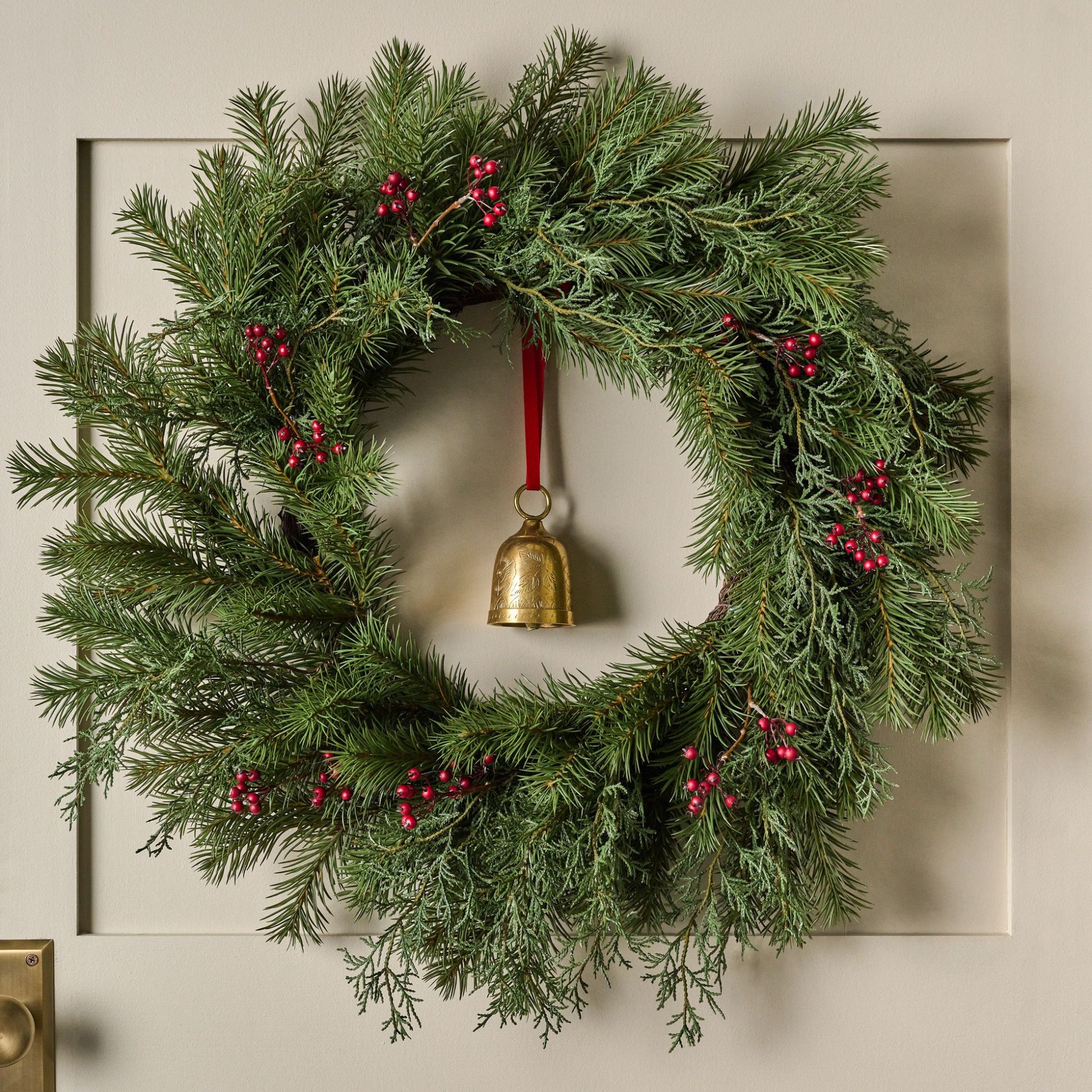 Real Touch Red Berry and Pine Wreath mot en kremvegg.