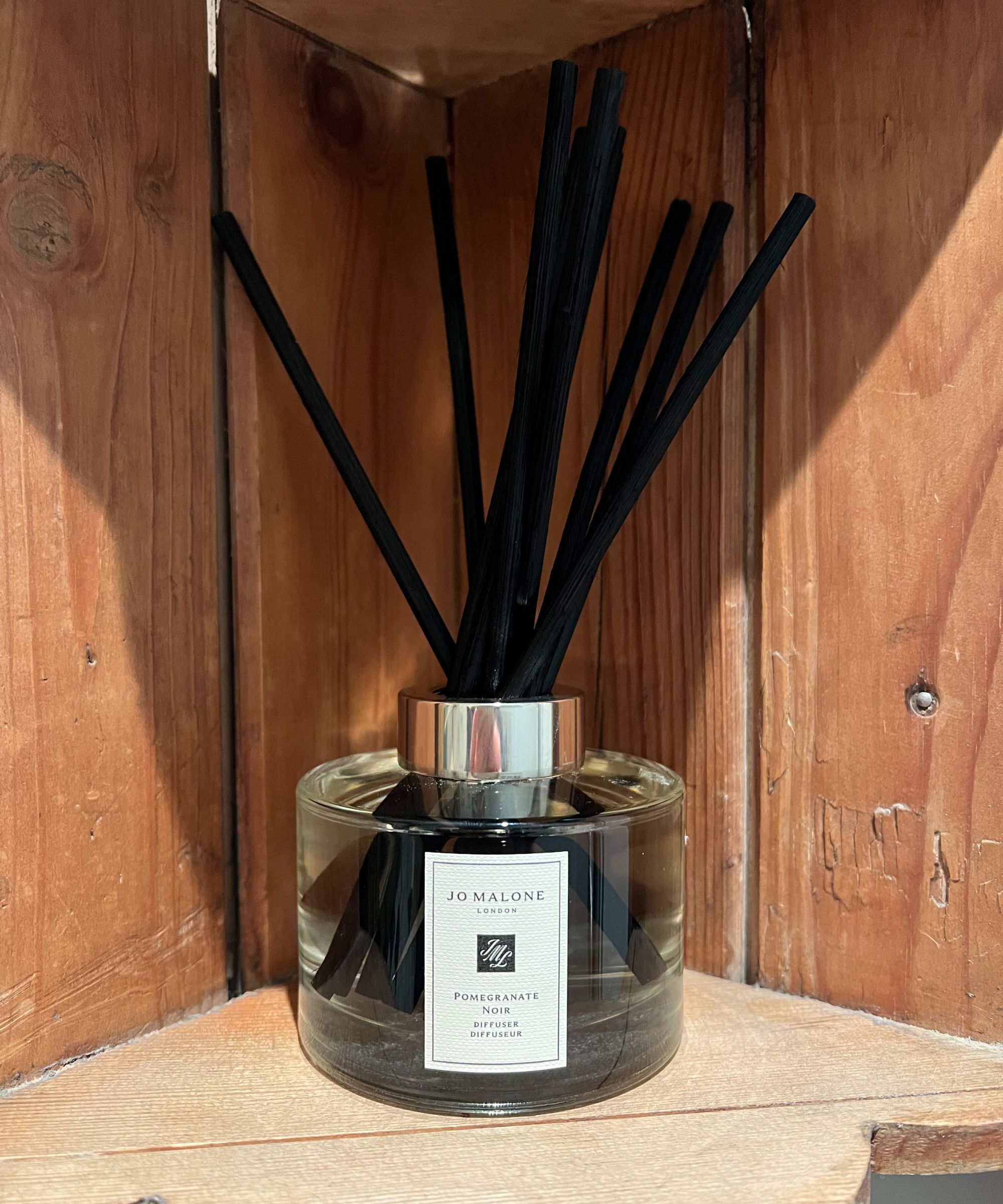 En Jo Malone granateple noir siv diffuser med svart siv på en antikk trehylle