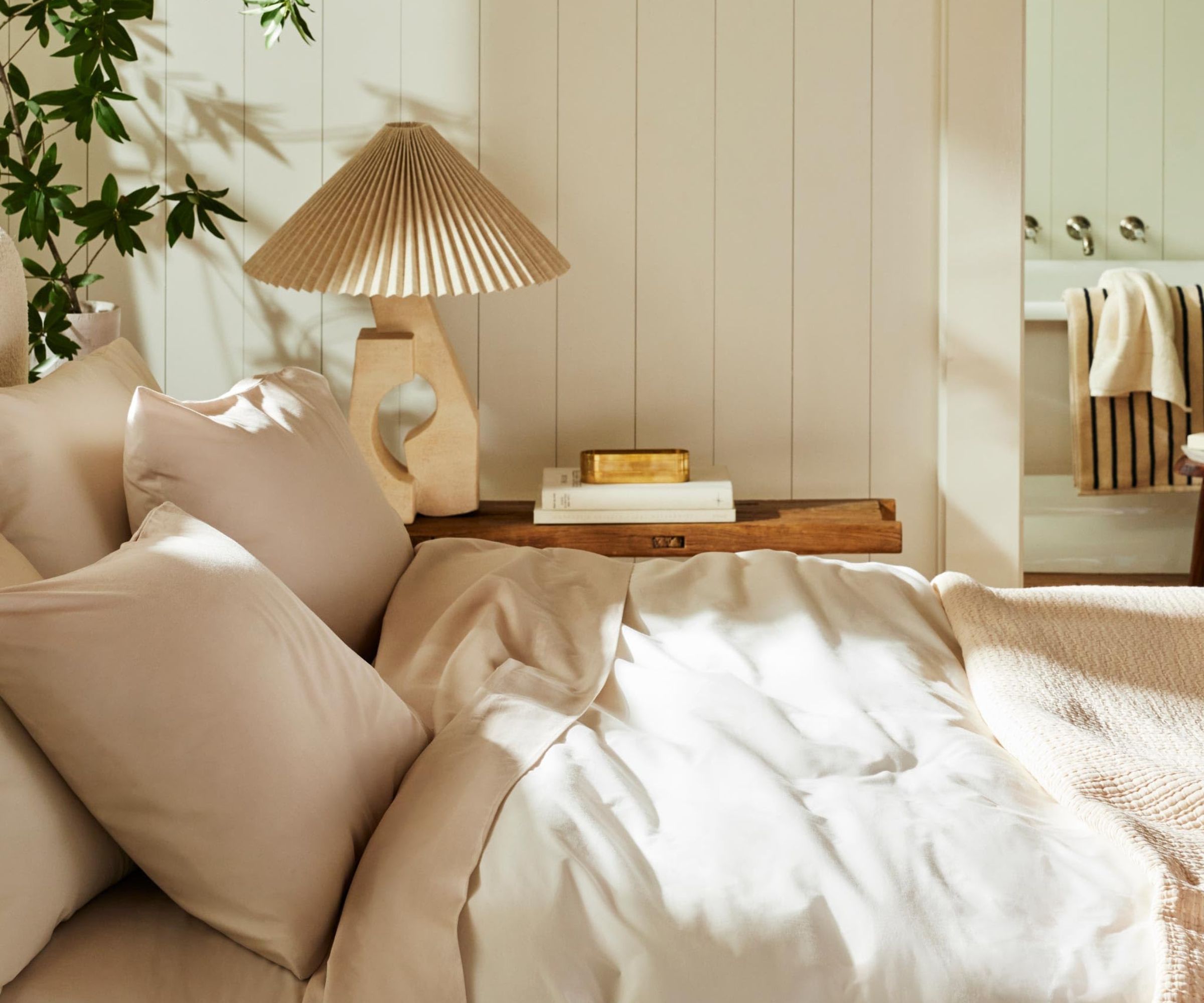 Sett fra siden av Brooklinen Luxe Sateen Sheet Set på en seng mot en kremvegg.