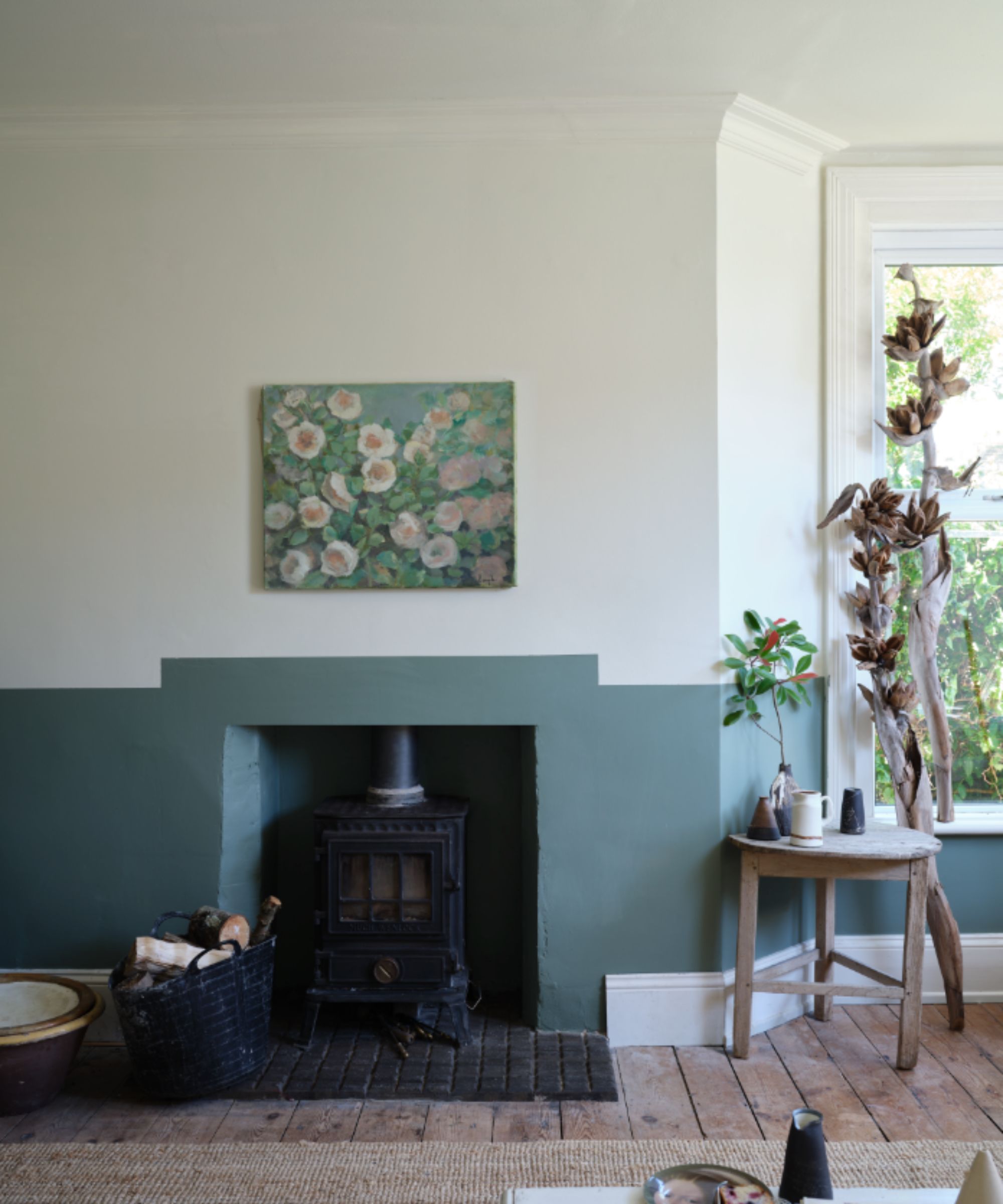 stue med grønn nedre halvdel av vegger, hvit øvre halvdel, peis med vedovn og tregulv, blomsterkunst over peisen