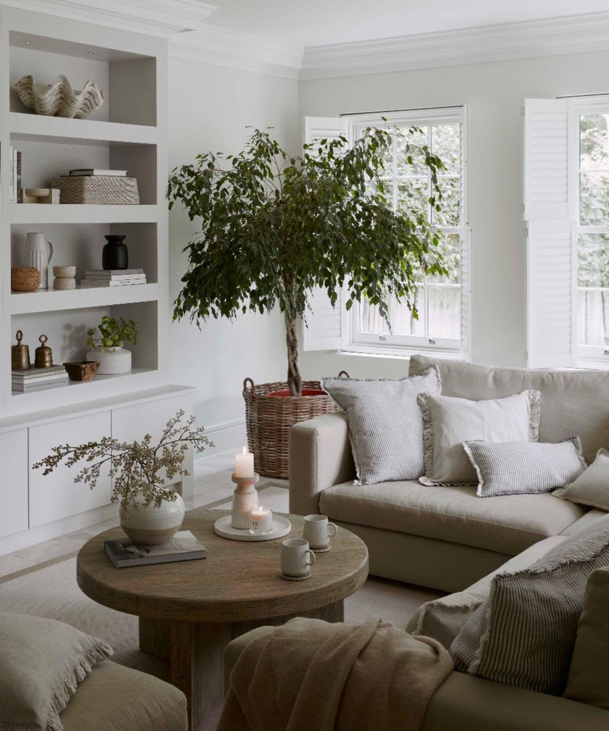 En stor skysofa med et stort oliventre, rundt tre salongbord og full stil bokhylle