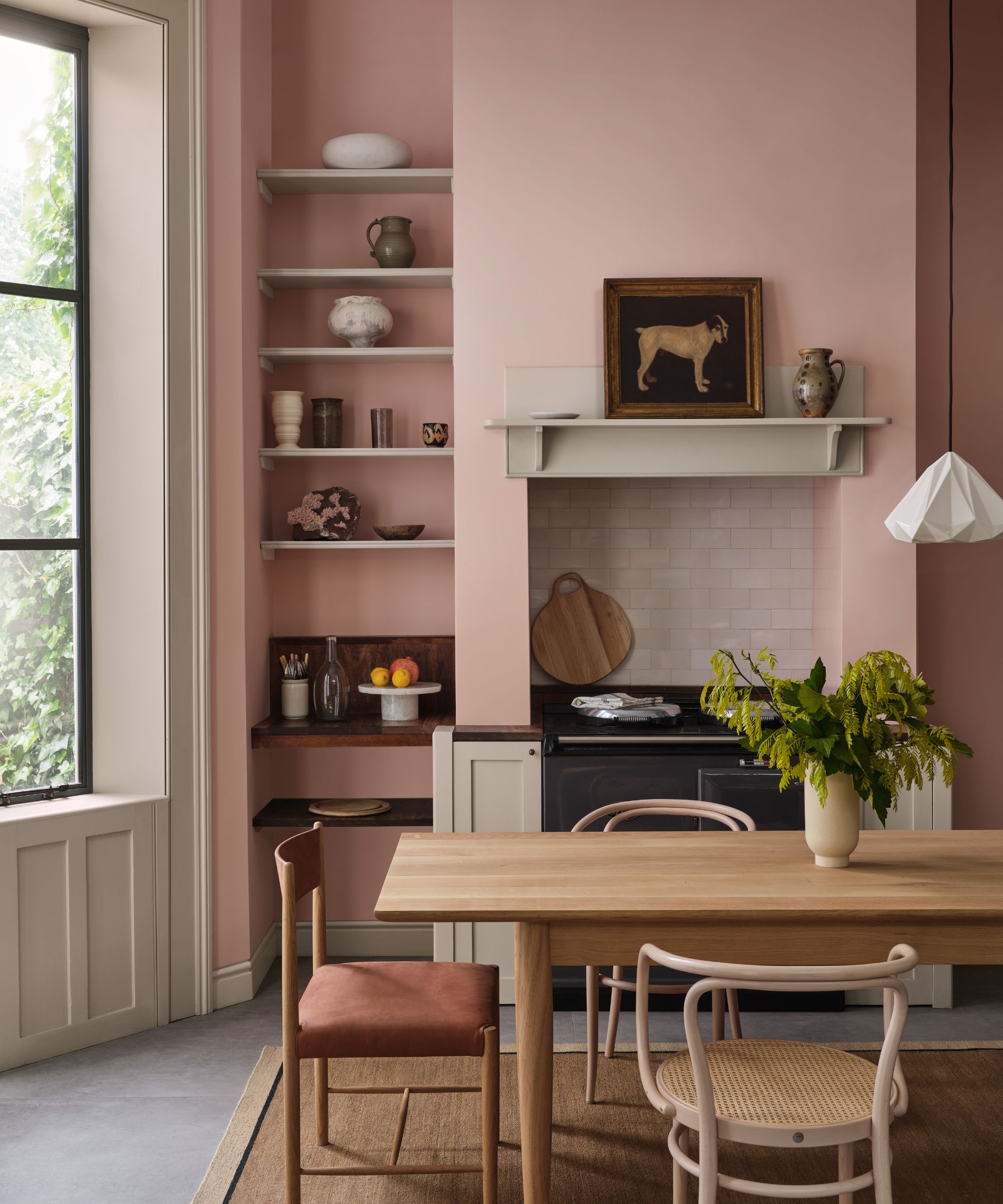 Kjøkken med rosa vegger, nøytral dekor og spisebord i tre med vas av løvverk