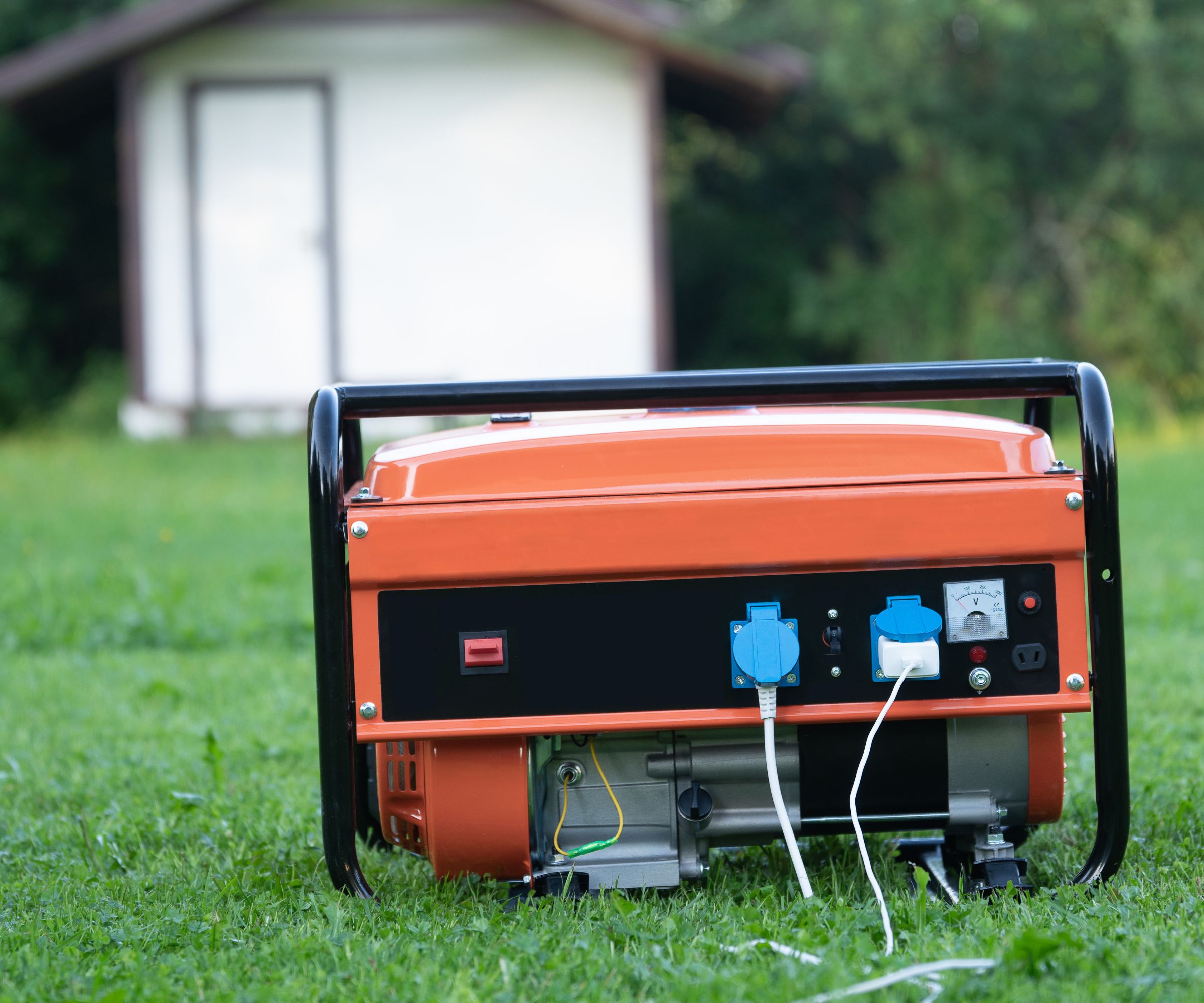 En oransje og svart bærbar generator ute på en kort gressplen