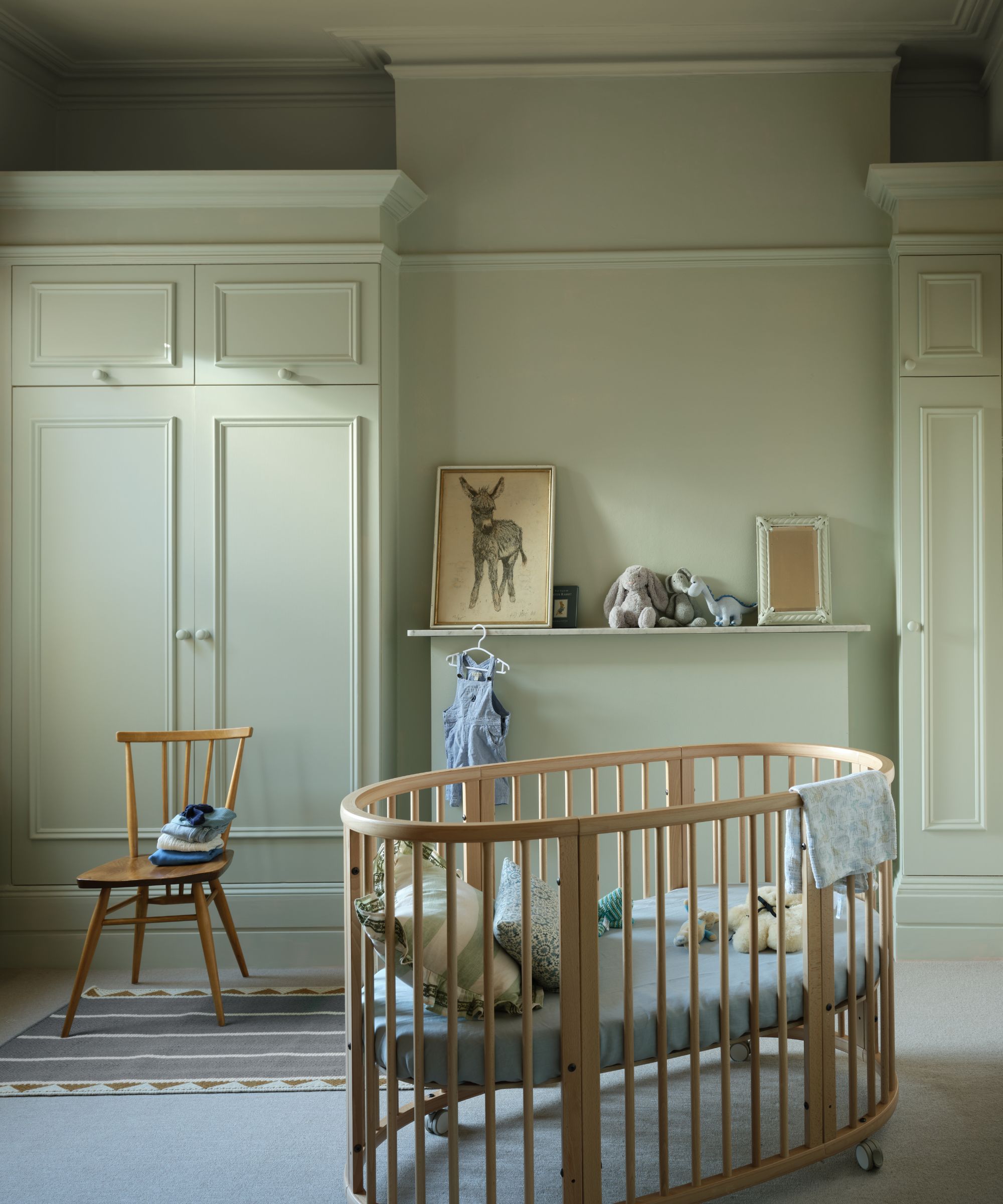 Nurserom med blekgrønne vegger, barneseng og stol