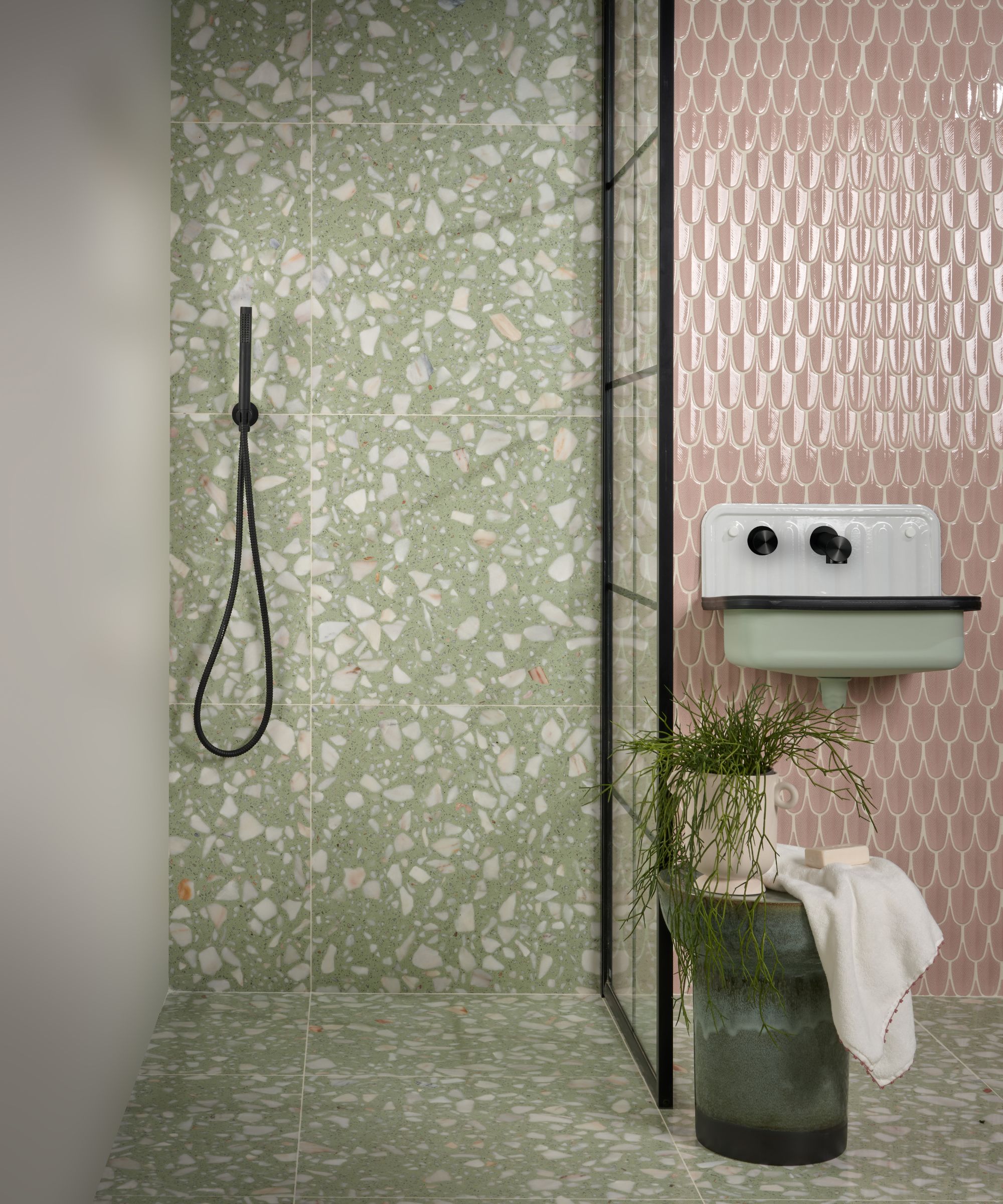 Et rosa og grønt bad med grønne terrazzo -fliser som drenerer dusjområdet og gulvet i hele badet og rosa veggfliser bak vasken