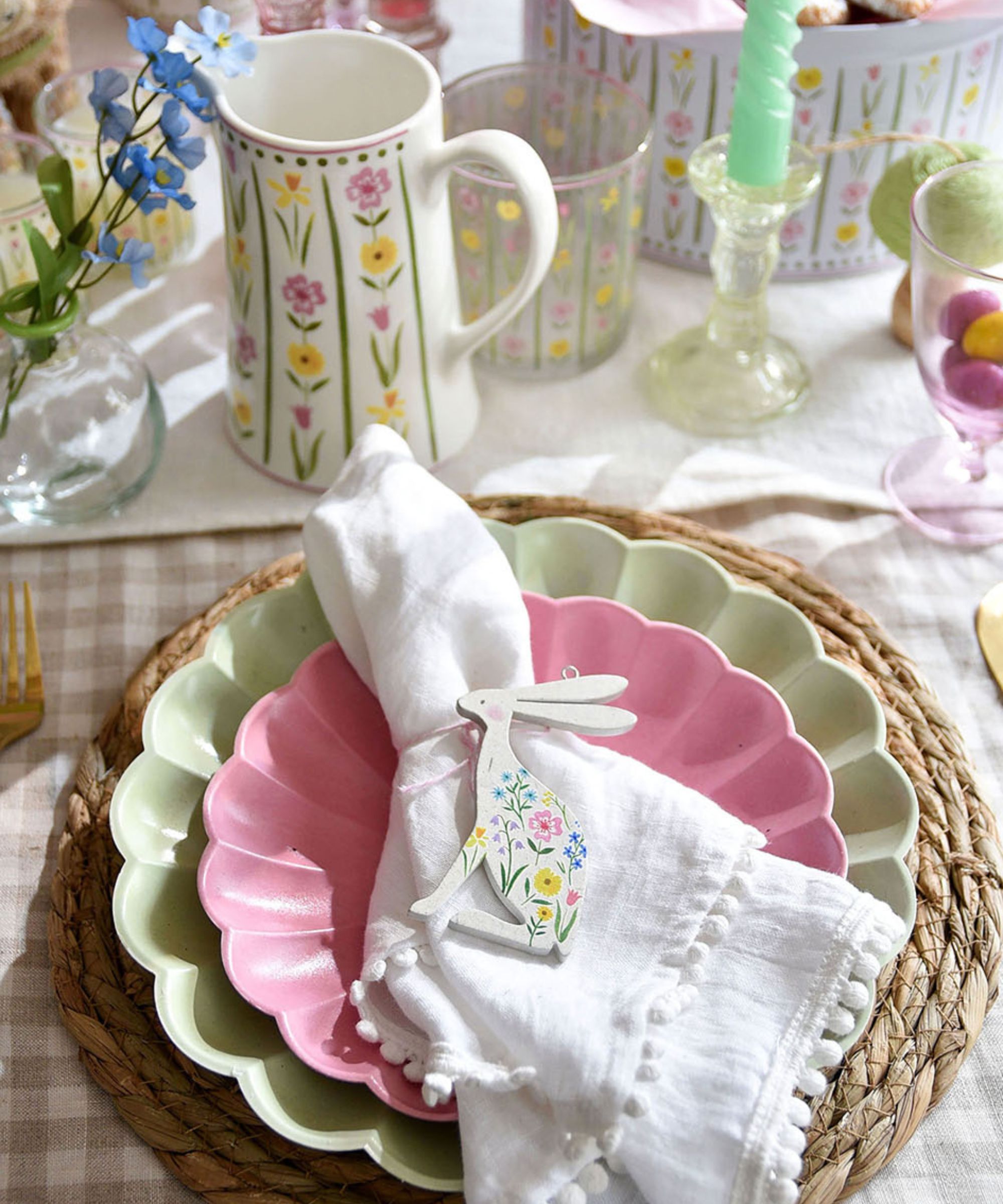 Påskebord med Gingham -duk, Rattan Placemat, grønne og rosa tallerkener og hvitt linserviett med bunny serviettring