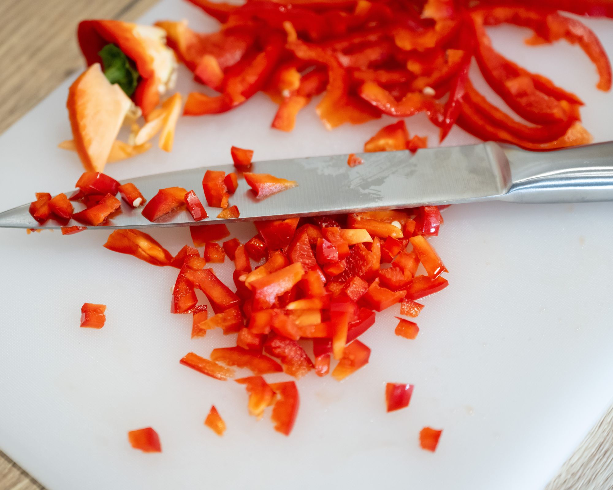 En sølvkniv som hviler på et hvitt hakkebrett med en hakket rød paprika på en lett treoverflate