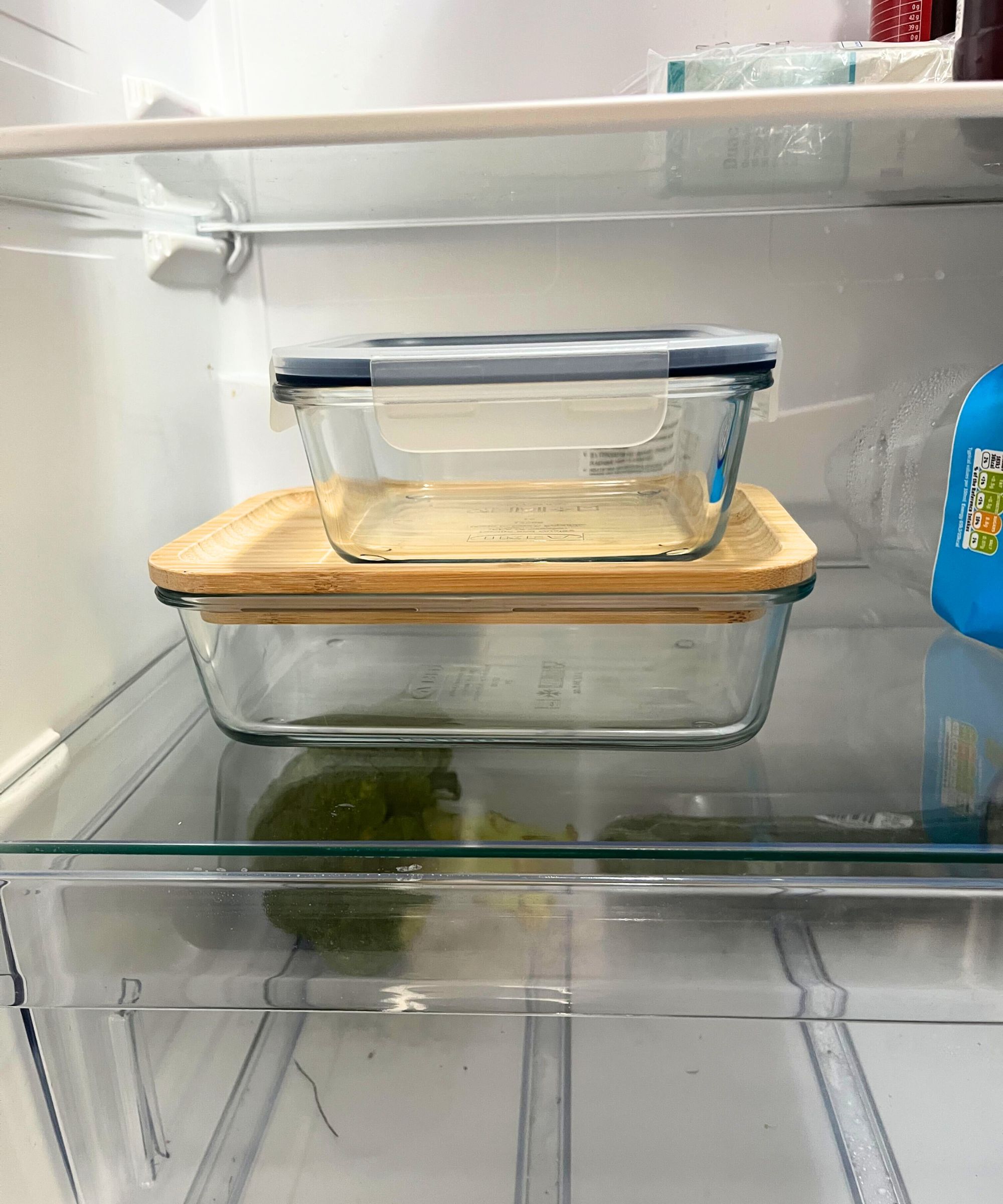 To glassmatbeholdere, en med et bambuslokk, en med et plastlokk, stablet på toppen av hverandre i et kjøleskap.