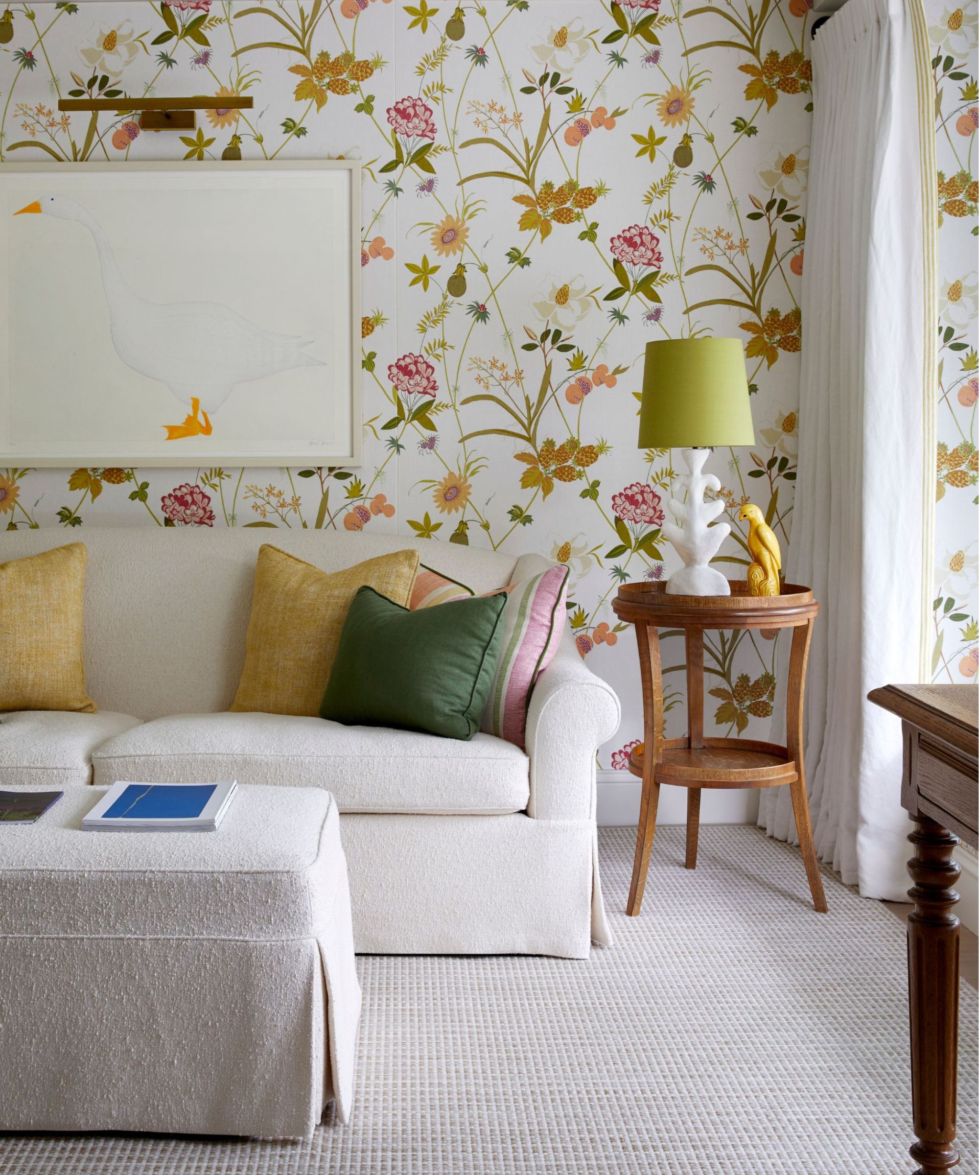 Stuen med blomsterrosa og gul tapet, en nøytral sofa med gule og grønne kastputer og vintage sidebord med en stor gåseveggkunst