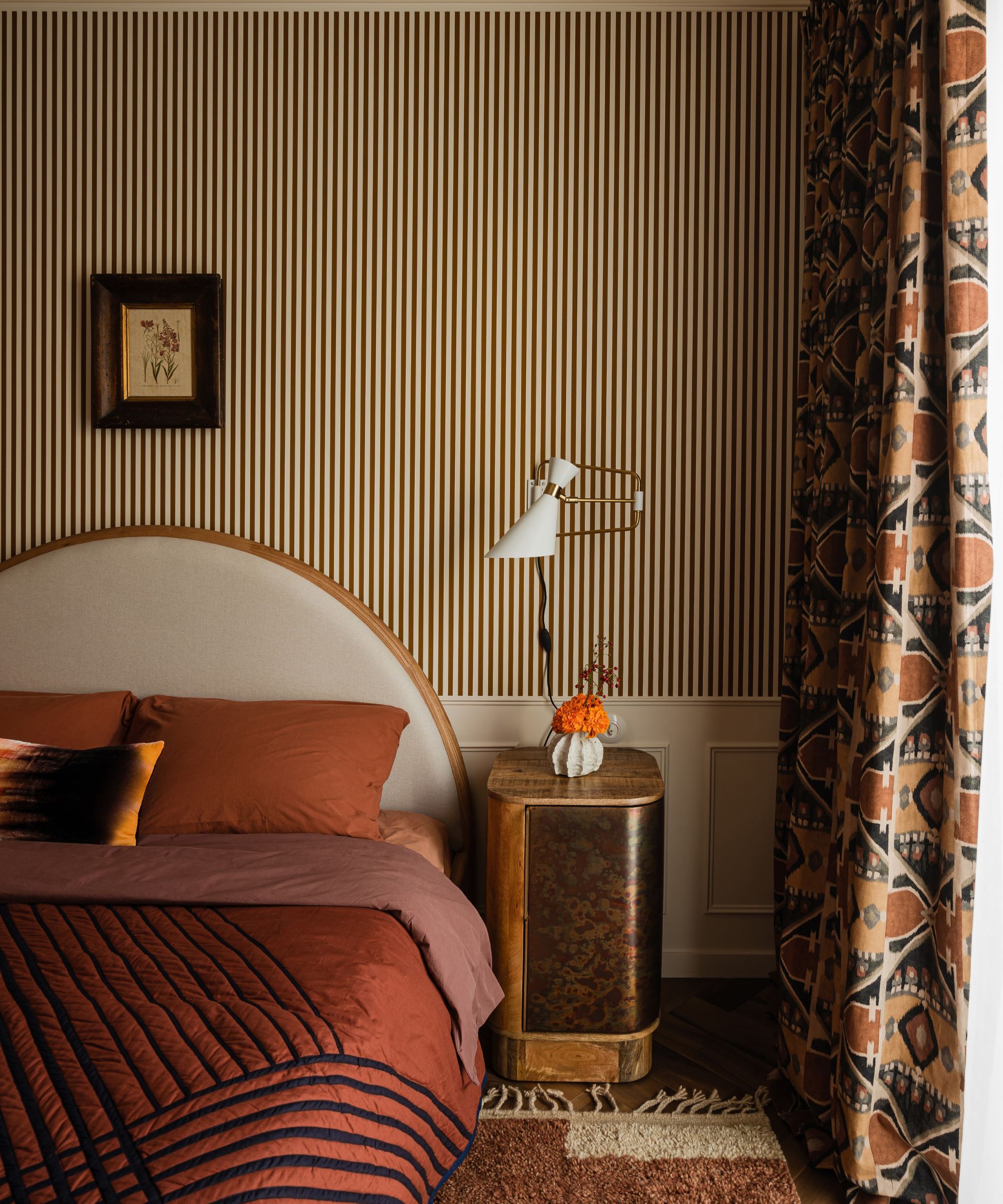 Art deco/ nouveau stil soverom med stripete bakgrunnsbilder, buet hodegjerde og oransje sengetøy, geometriske gardiner og burl tre og gull sengebord