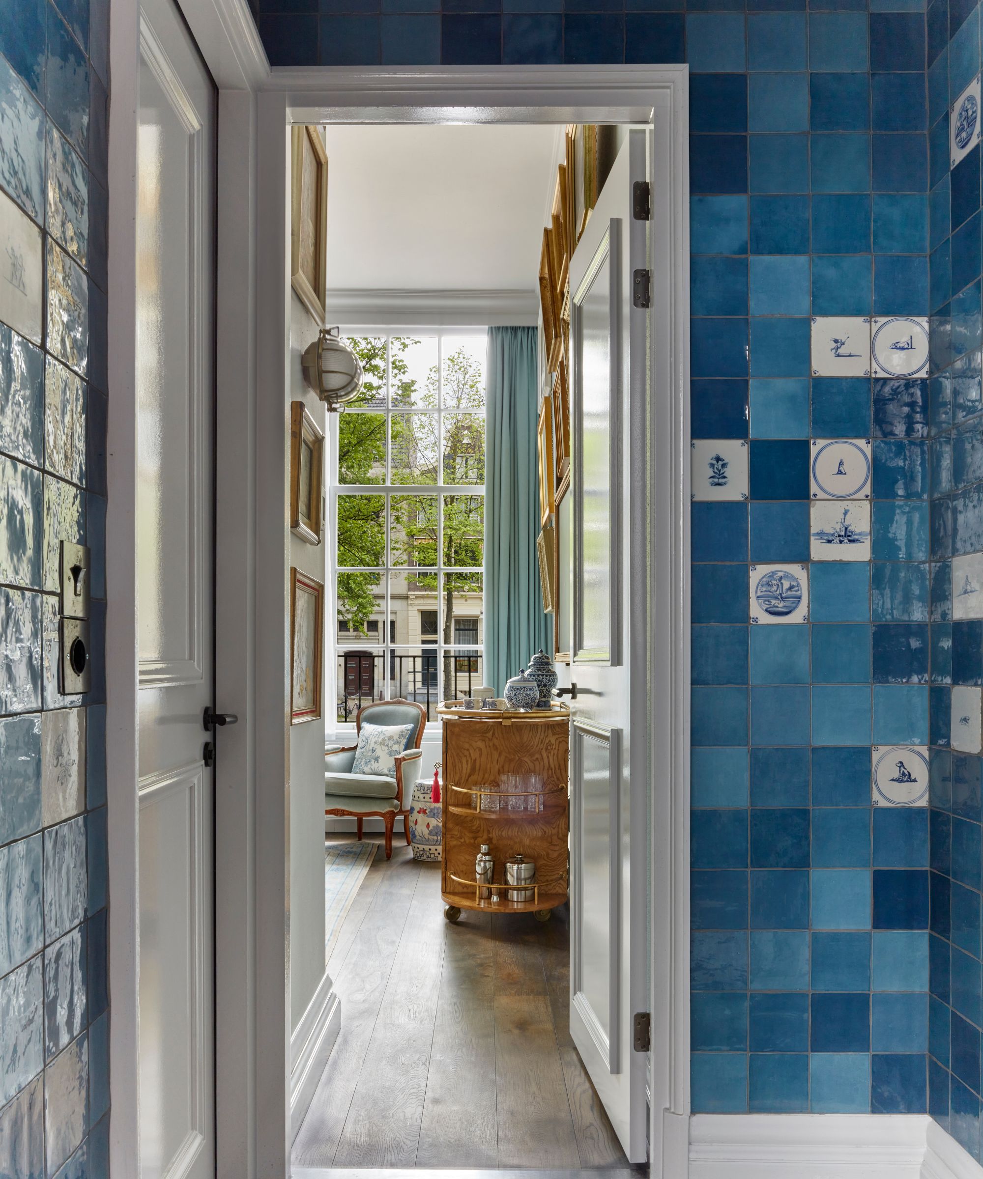Hotellbad med blå zelige -fliser og en håndfull håndmalte Delft -fliser i blandingen med utsikt gjennom døren inn i hovedsoverommet Suite