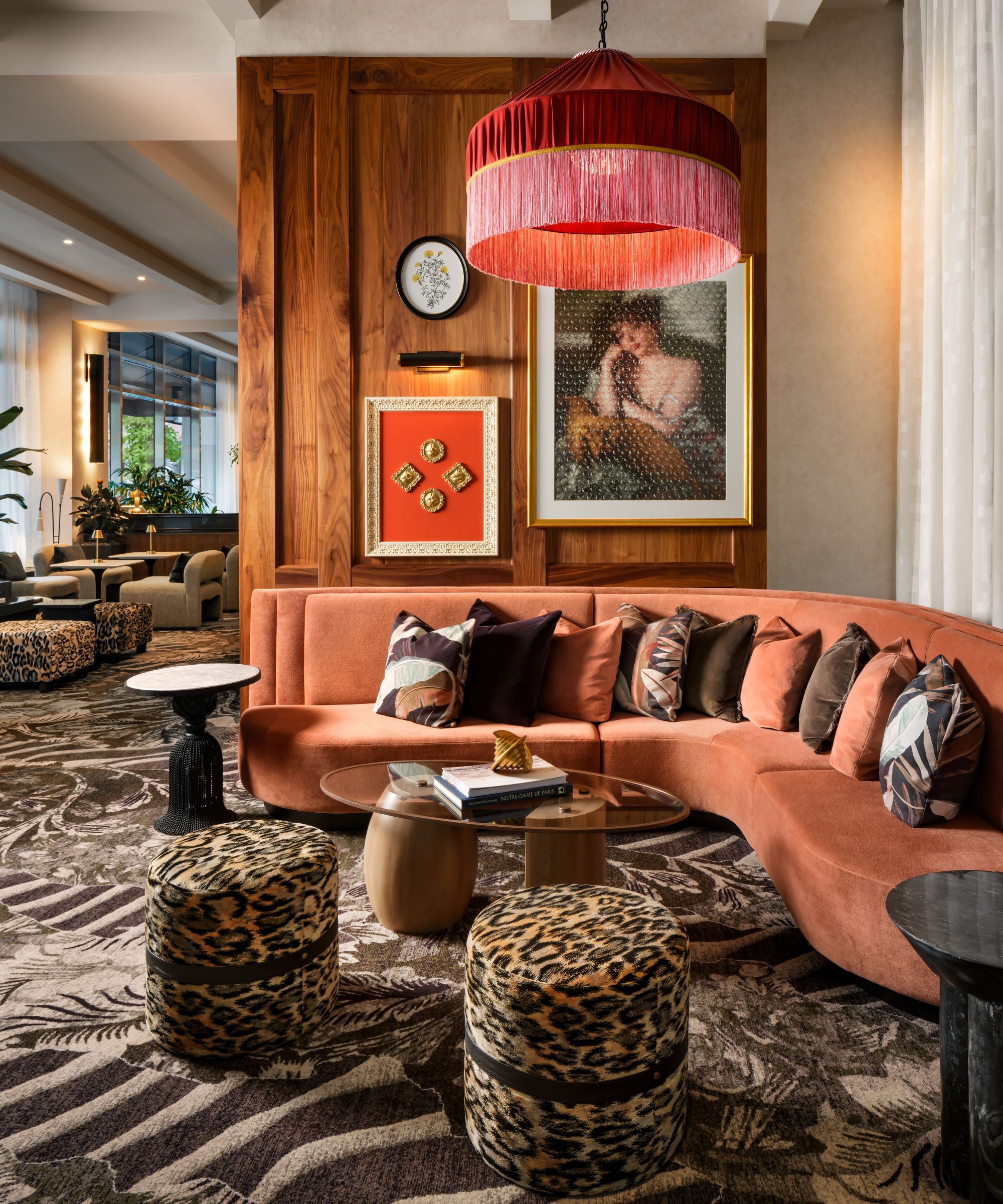 Hotelllounge lobbyområde med trepanelvegg, et stort rosa frynselys hang over en oransje fløyels buet sofa med lite leopardtrykk osmannisk avføring og mønstret teppe
