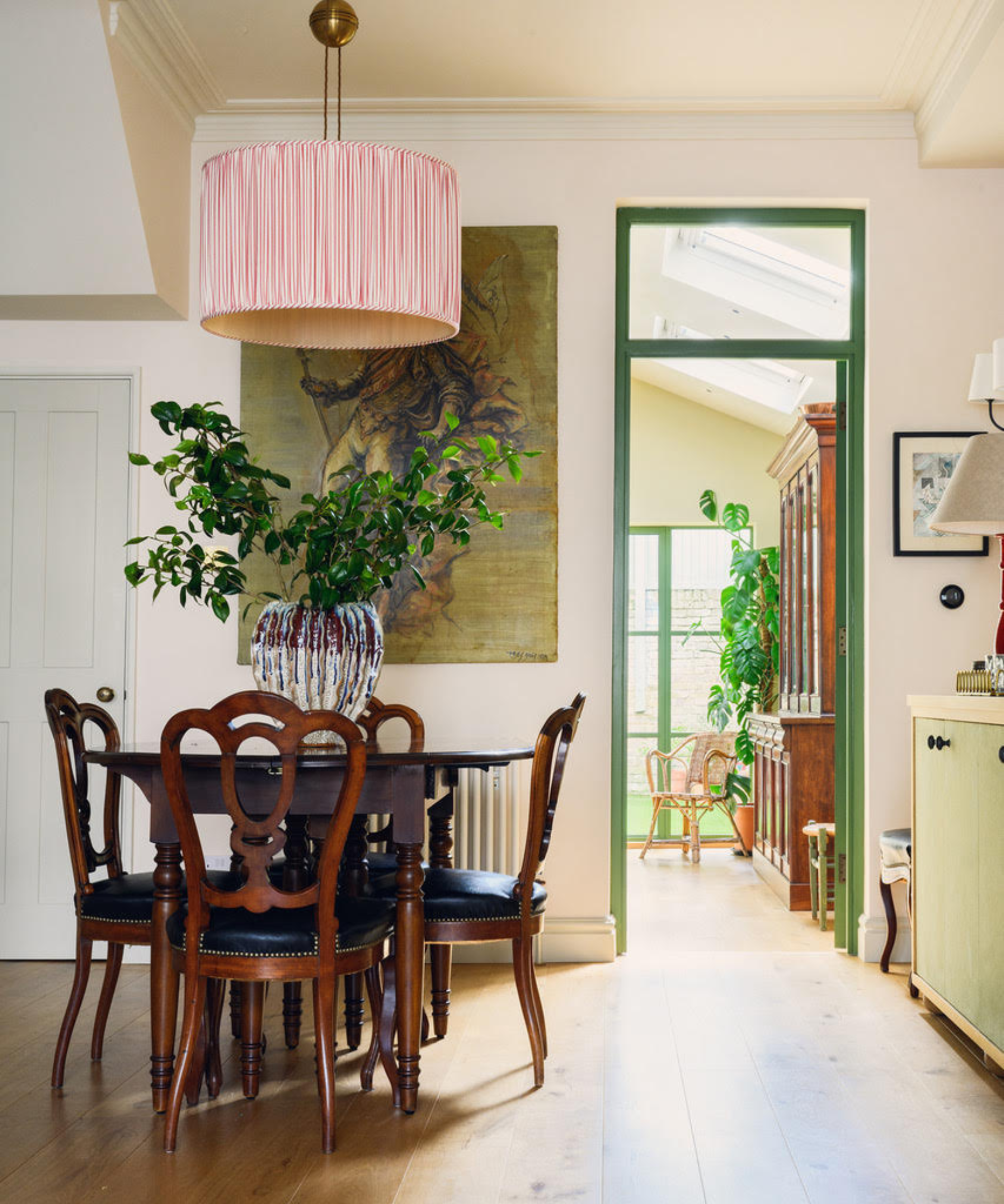 Spisestue med vintage trebord og stoler og en stor vase med grøntområder
