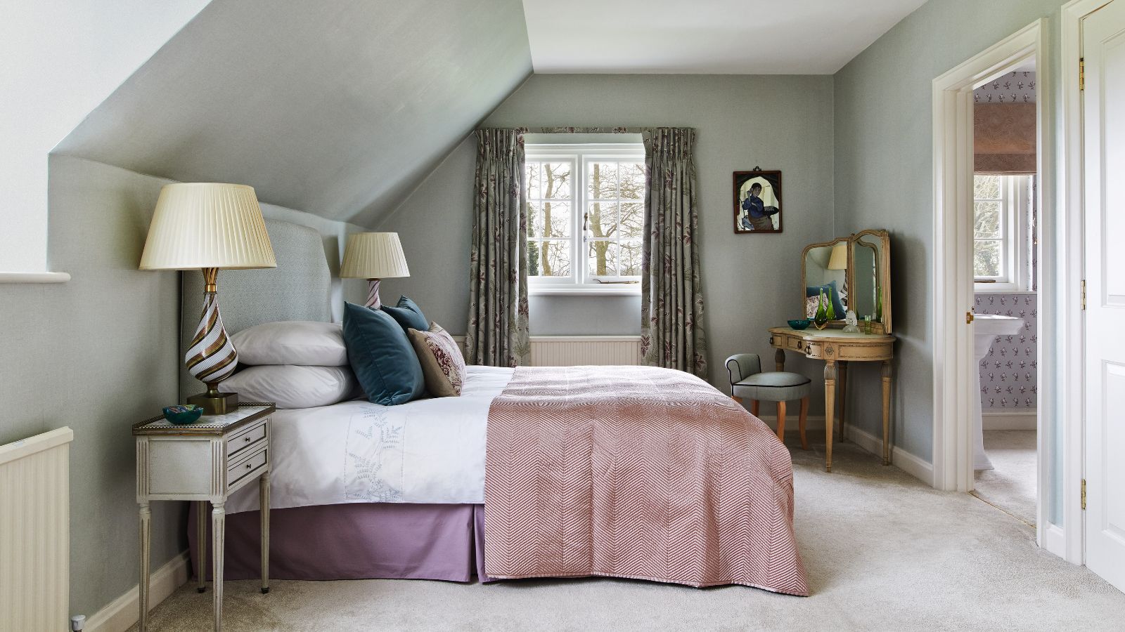 Bedroom with grey carpet, large bed with pink throw and beside tables with striped lamps