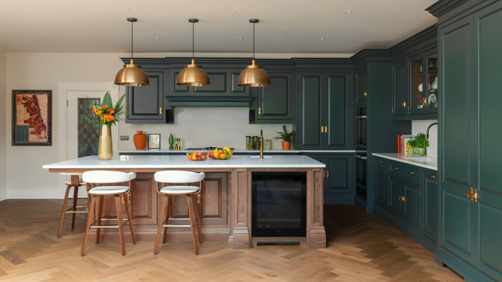 A traditional blue-green kitchen with a wooden island and white barstools. Three brass pendants above.