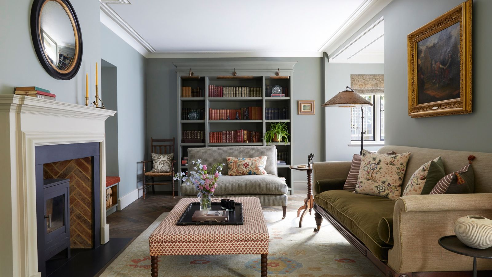 Vintage living room with fireplace, upholstered ottoman, cream sofa and vintage art and bookcase