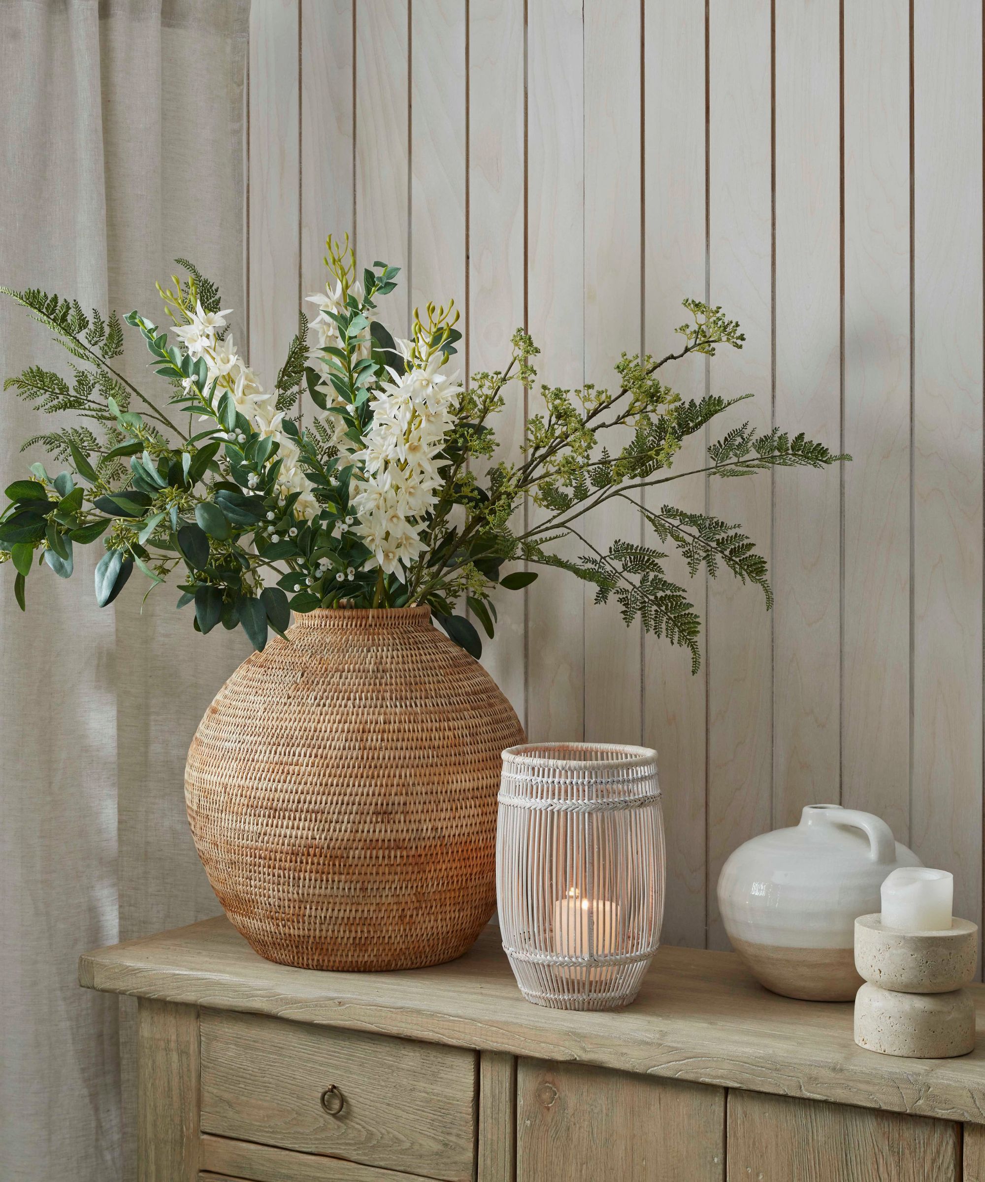 En stor vase med hvite vårblomster på et sidenbord ved siden av en liten kurvholder