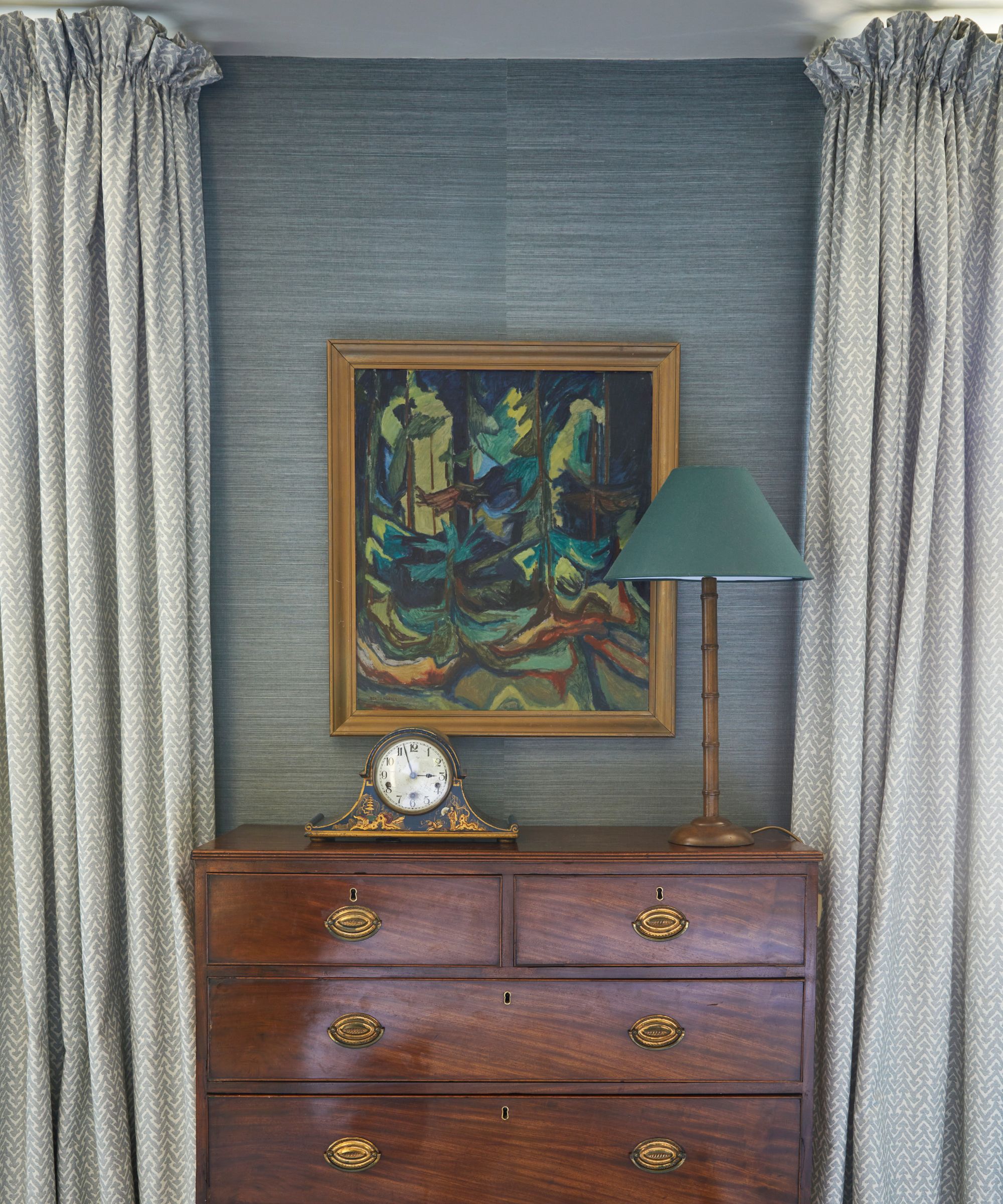 En antikk kommode med en vintage klokke, en høy lampe og et innrammet bilde som henger over