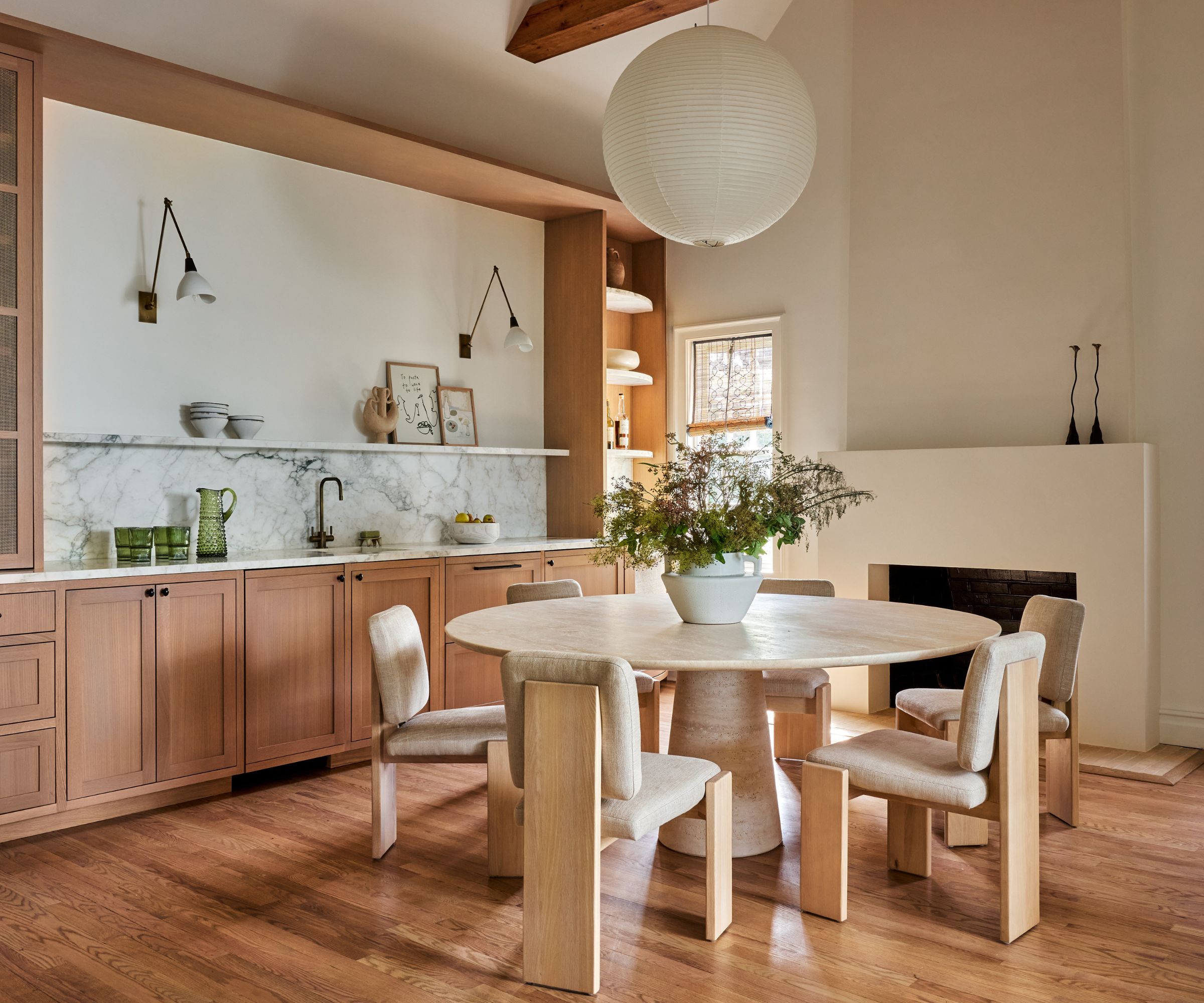 Spisestue med marmor rundt bord, bukelstoler, tre skap og marmor backsplash og lyktelys