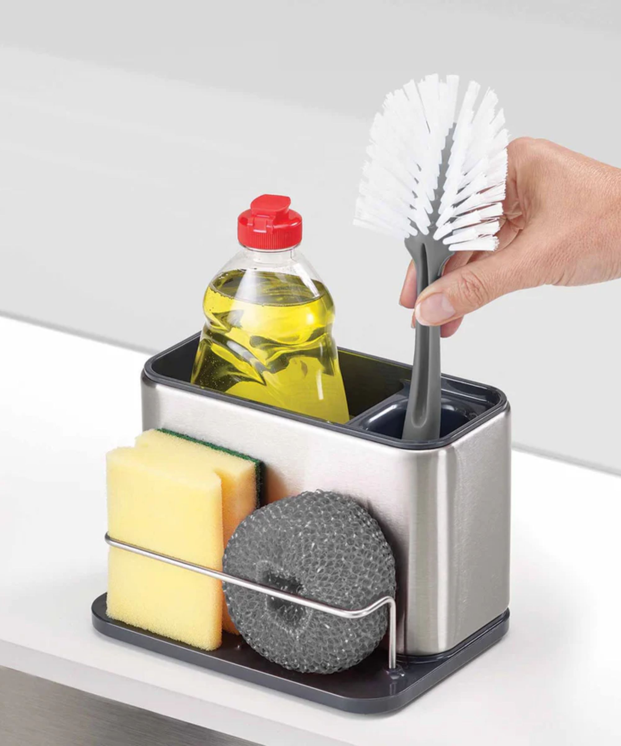 En sølvvaske som organiserer caddy med gul oppvasksåpe, en skrubbebørste og skuringssvamper.