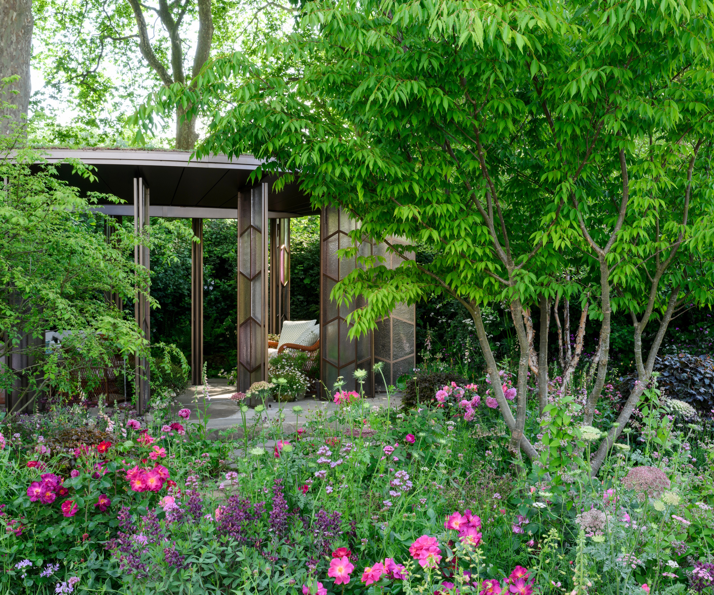 Et moderne glasshus med rosa, lilla og syrinplanting i forgrunnen
