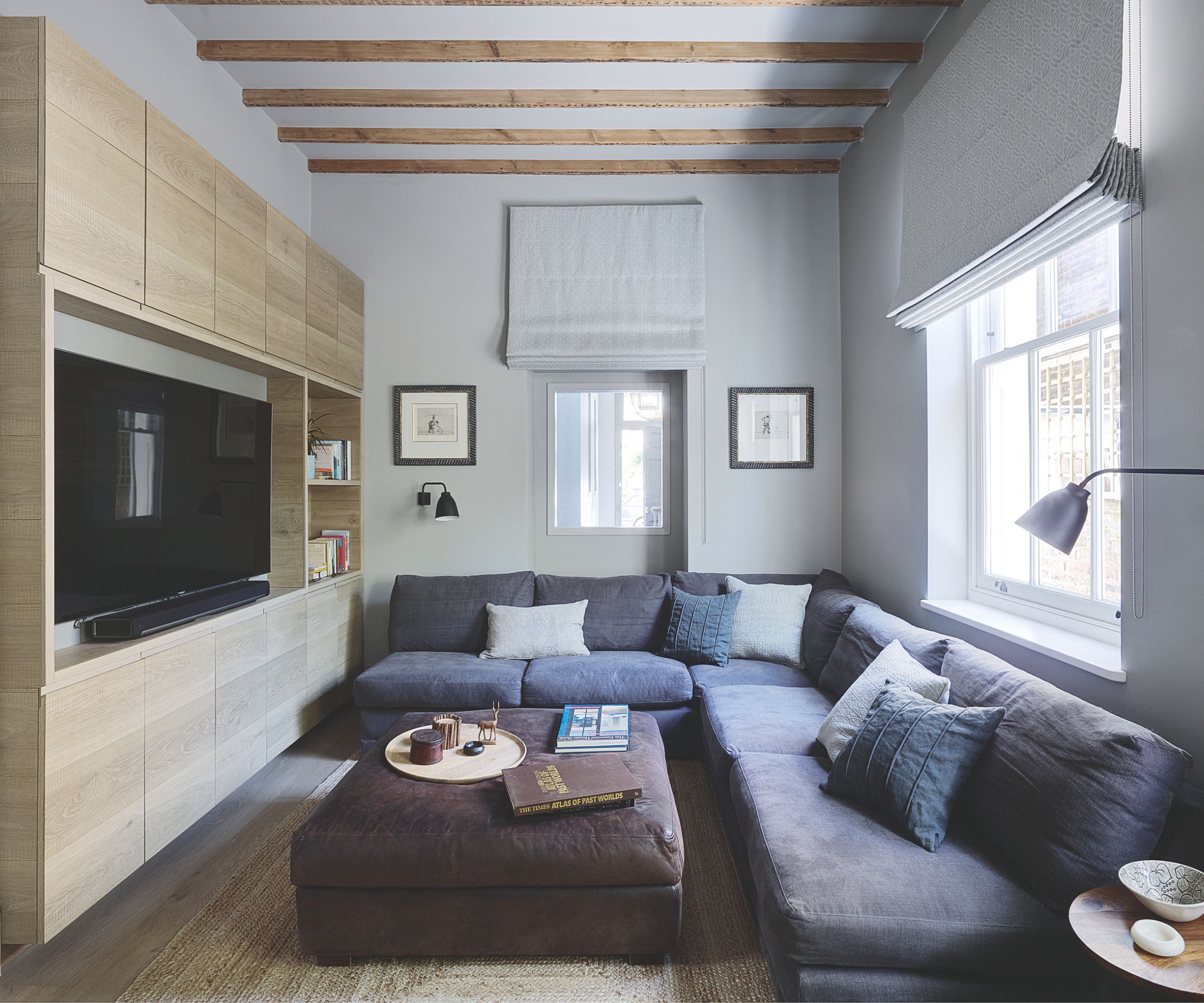 Stue med L -formet sofa, mediekonsoll med TV, ottoman og bjelker