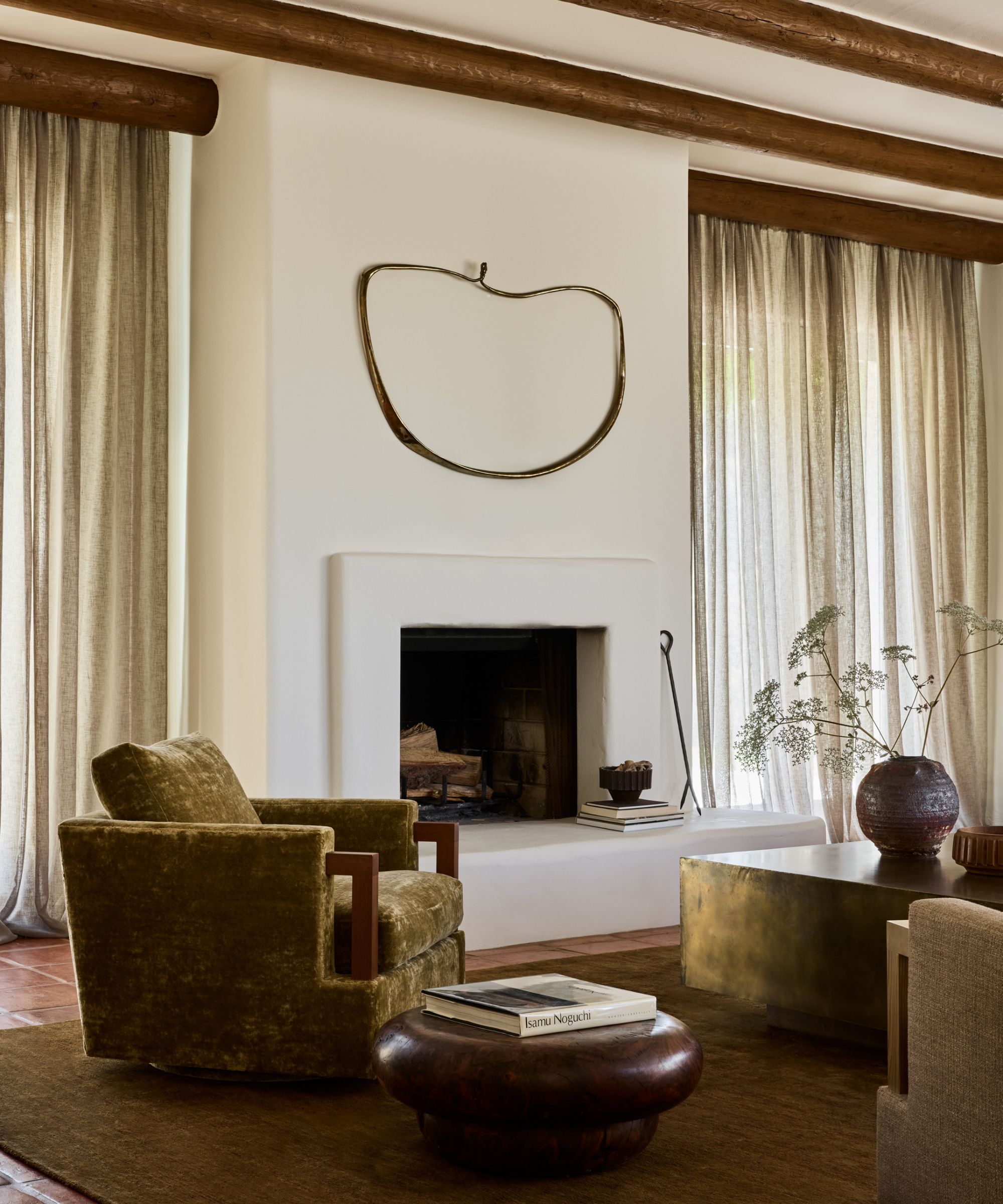 En Adobe Home Living Room med hvite pussede vegger, jordnær grønn lenestol og et rundt trebord på tre