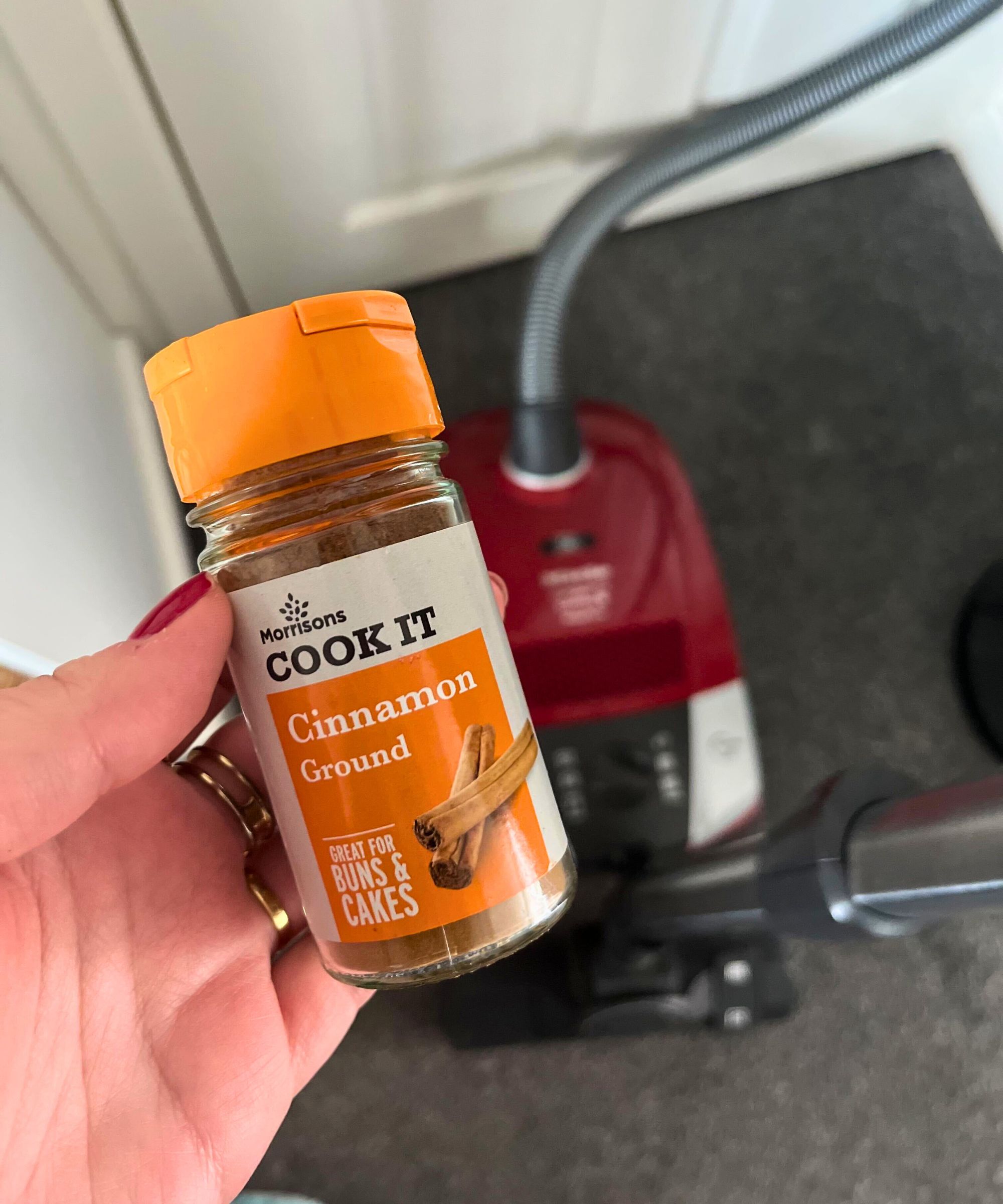 Krukke med malt kanel holdt over Miele Canister -vakuum på grått teppe